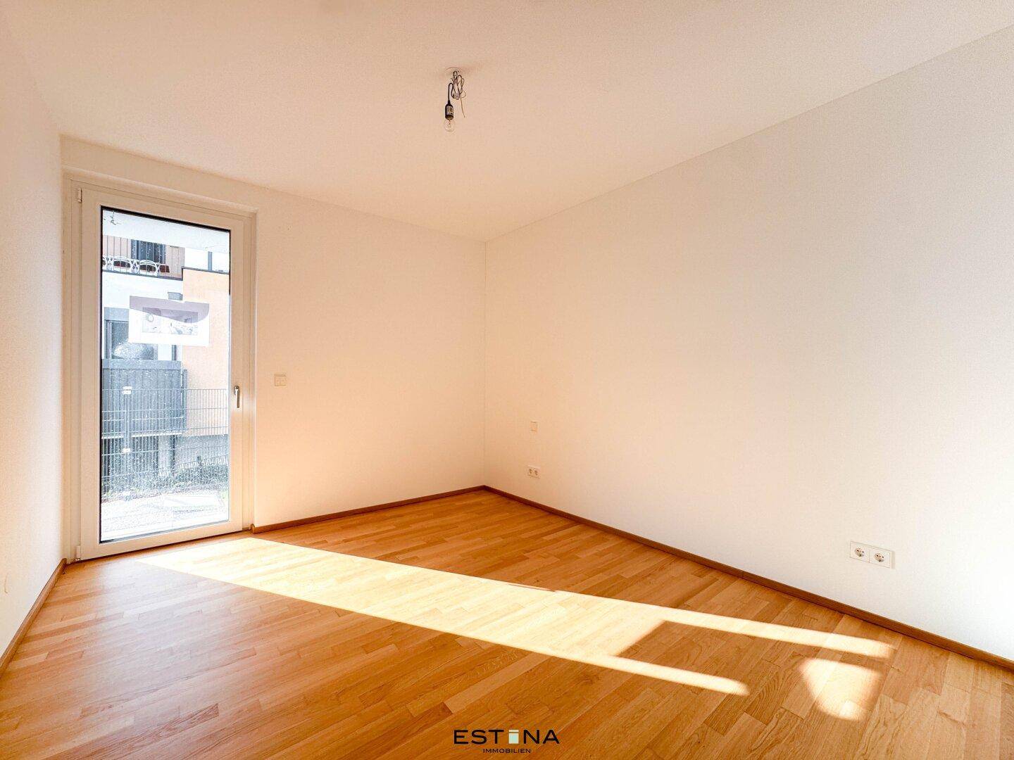 Helles Schlafzimmer mit Parkettboden und Zugang zu einem Balkon oder einer kleinen Terrasse.
