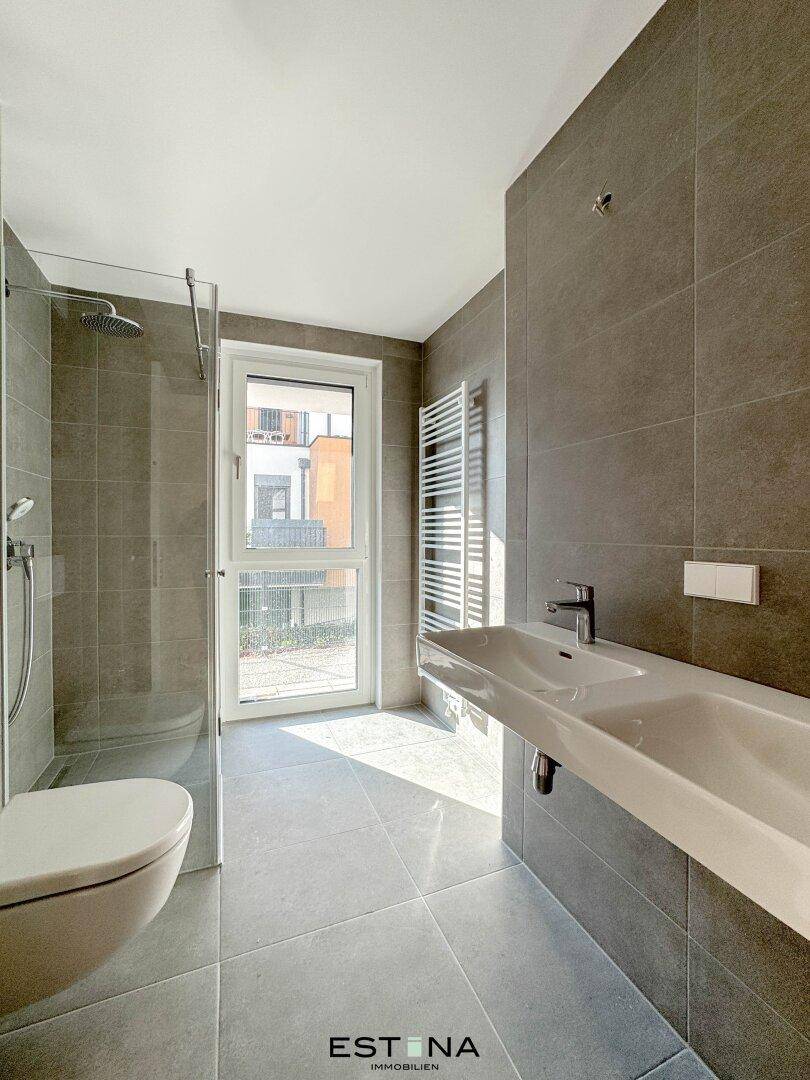 Modernes Badezimmer mit großer Dusche, Doppelwaschbecken und Fenster für Tageslicht.