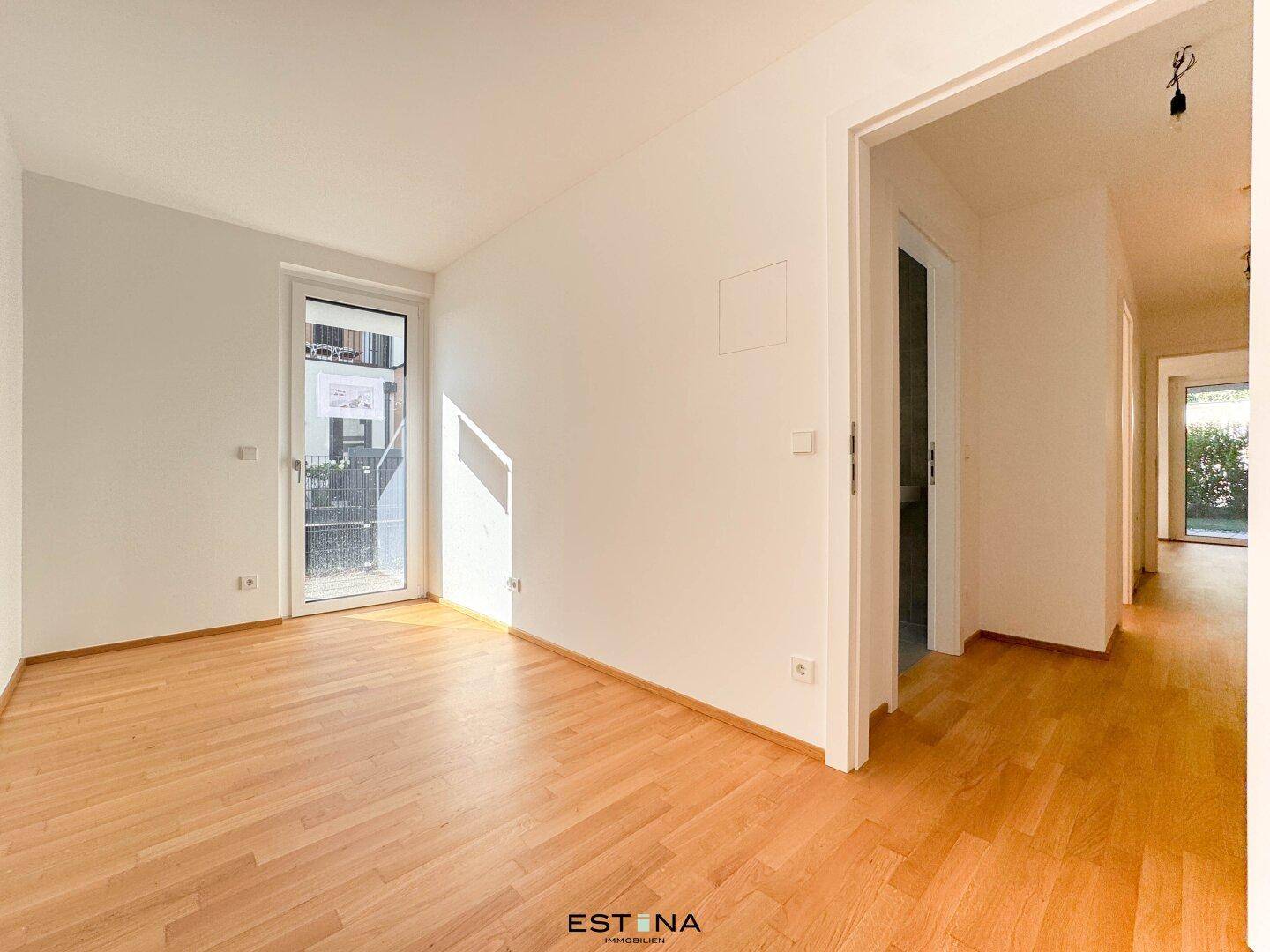 Heller Raum mit Parkettboden und Zugang zum Außenbereich, verbunden mit einem Flur.