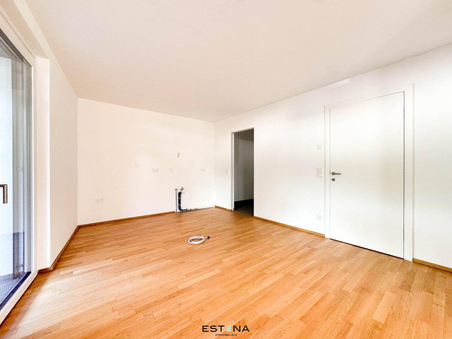 Leerer Küchenbereich mit Anschlüssen und Parkettboden, bereit für die Installation einer Einbauküche.