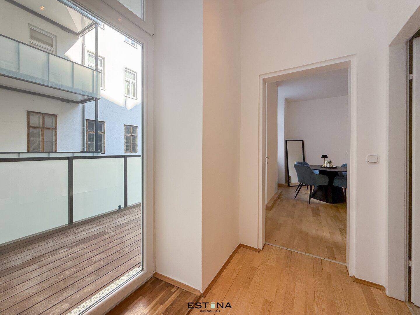 Heller Flur mit Zugang zum Balkon und Blick in den offenen Wohnbereich, schafft eine einladende Atmosphäre.