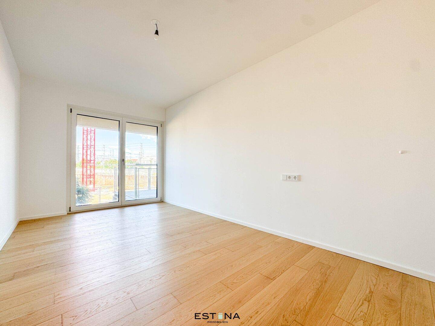 Helles Schlafzimmer mit Parkettboden und Zugang zu einem französischen Balkon.