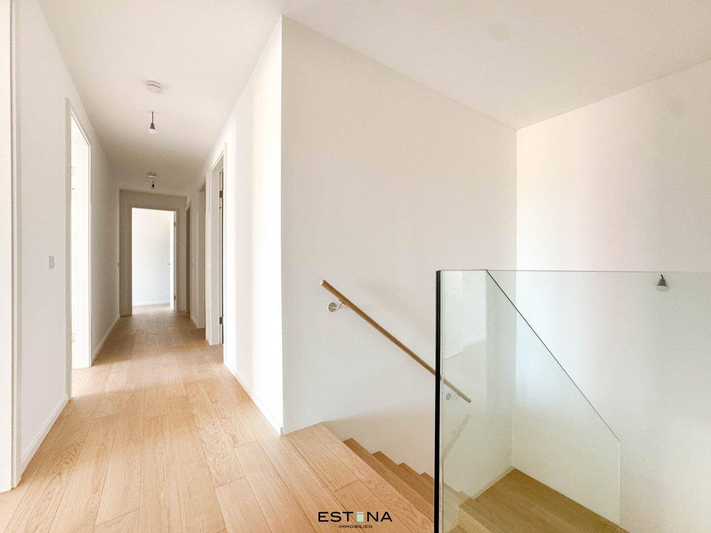 Heller Flur mit Holzfußboden und moderner Treppe mit Glasgeländer.