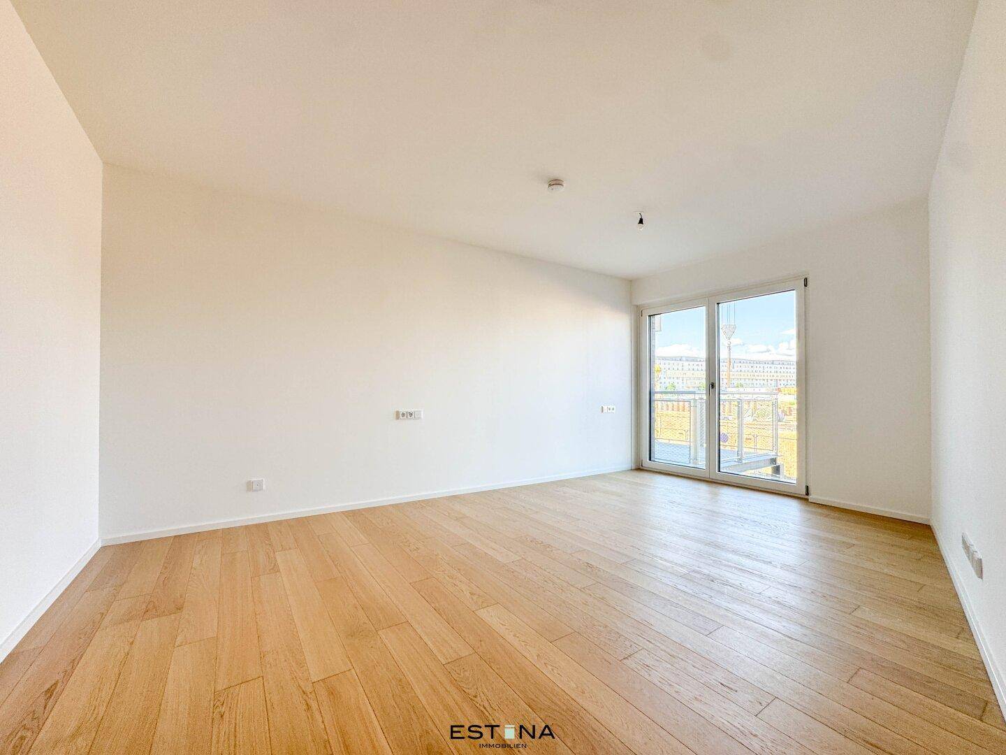 Lichtdurchflutetes Zimmer mit Holzboden und großem Fenster zum Balkon.