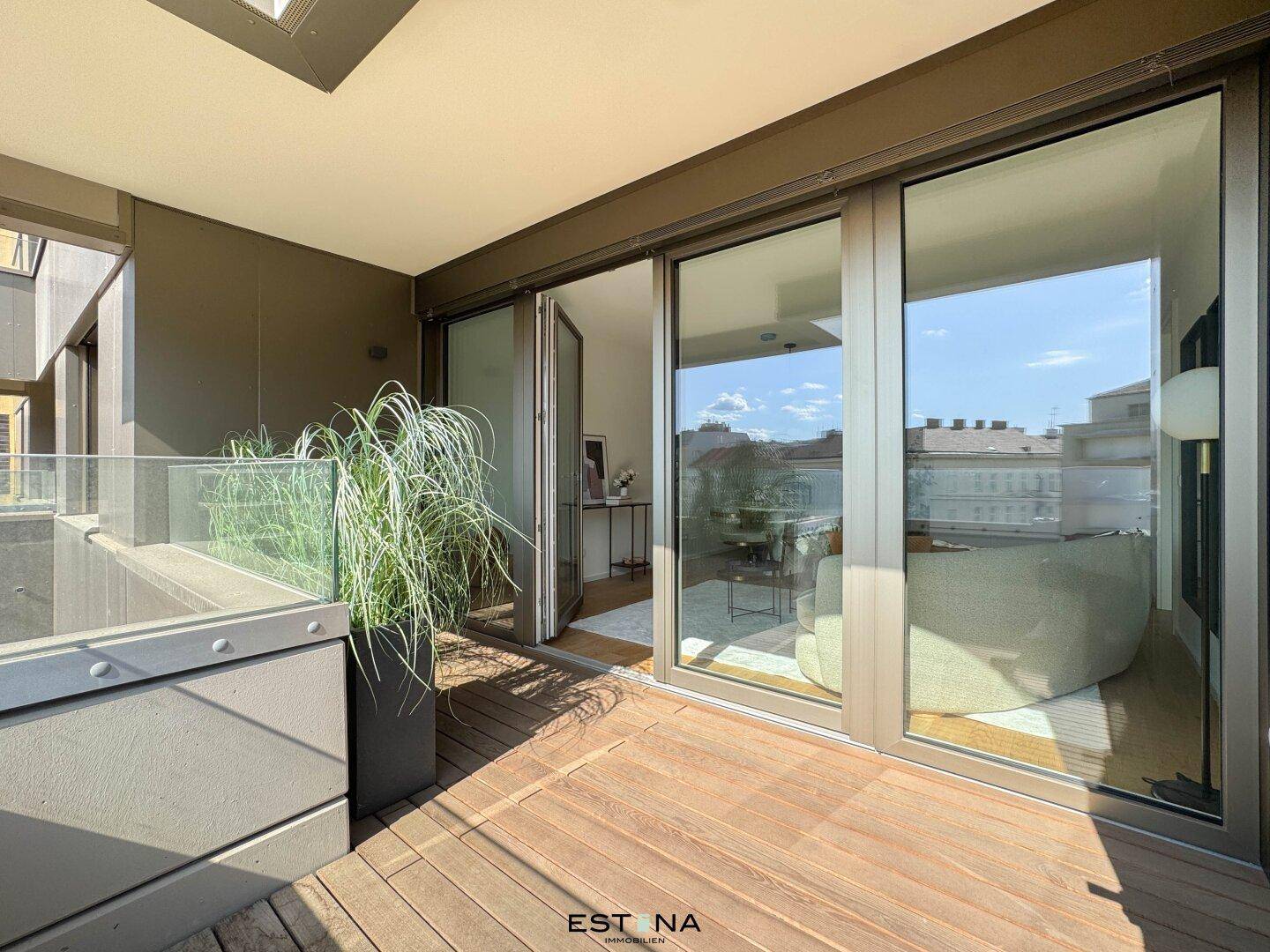 Sonniger Balkon mit Holzboden, Glasbrüstung und Blick auf die Umgebung.