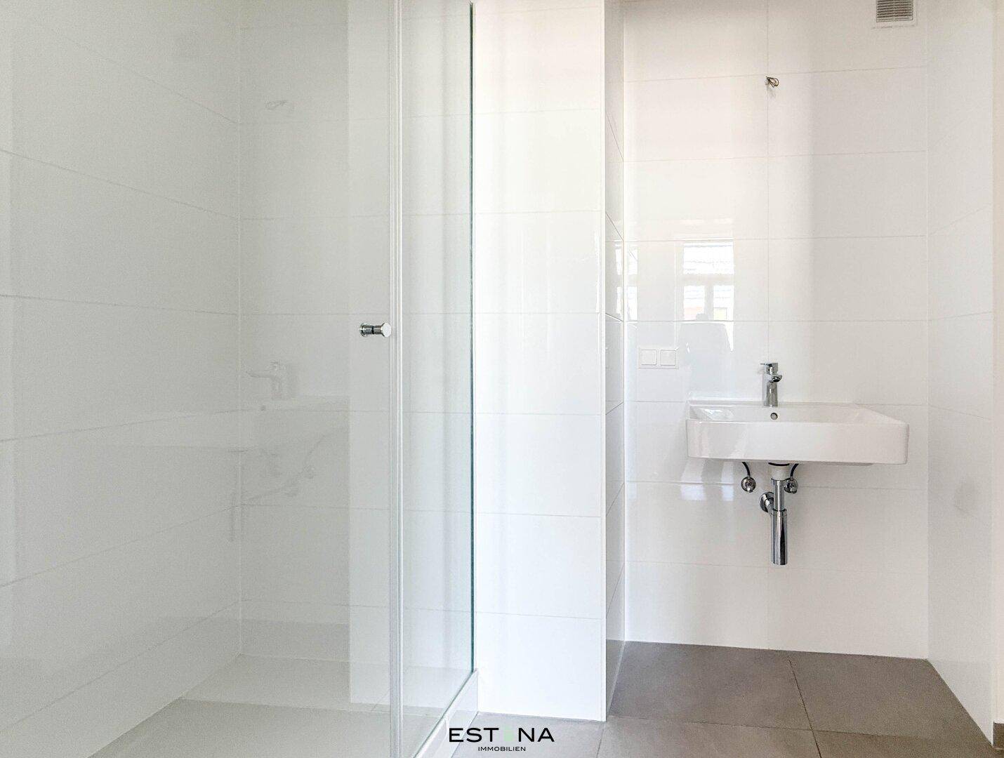 Modernes Badezimmer mit weiß gefliesten Wänden, ebenerdiger Dusche und Einzelwaschbecken.