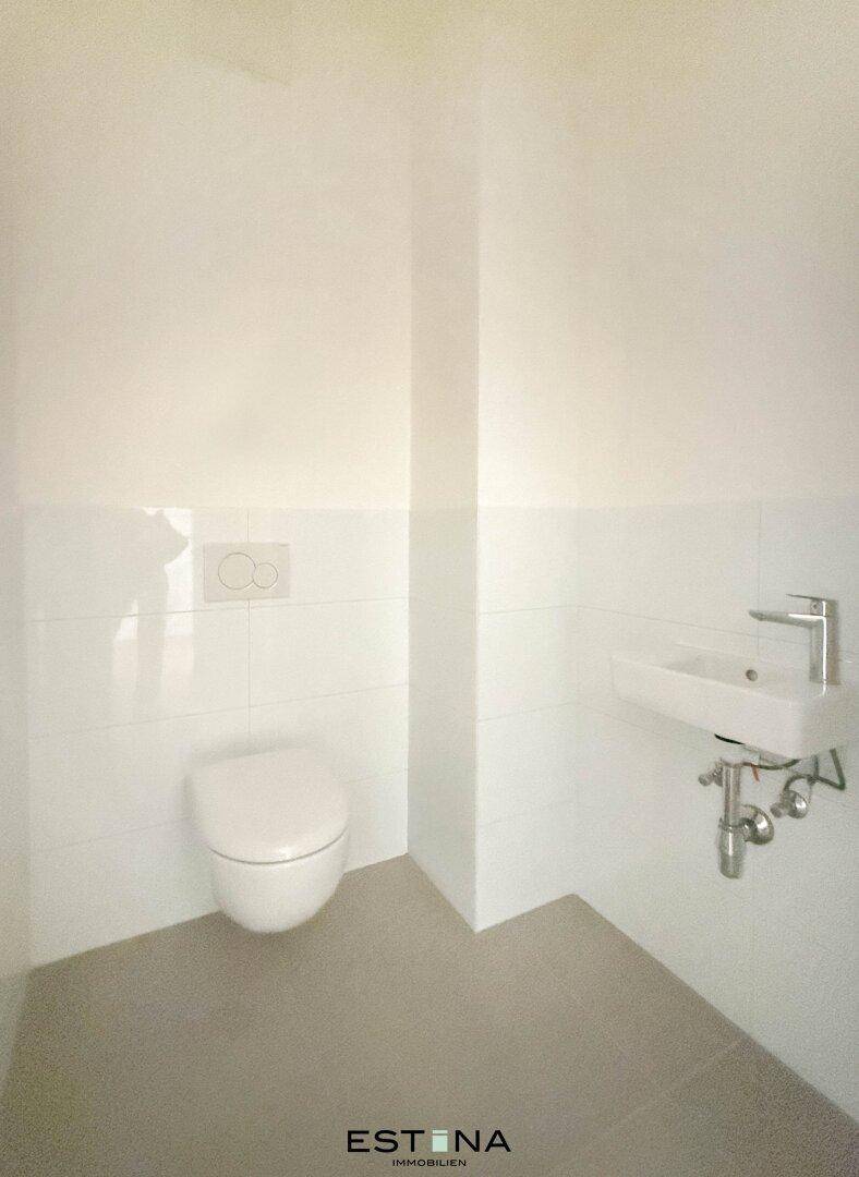 Kleines, funktionales Gäste-WC mit wandhängender Toilette und Waschbecken, hell gefliest.