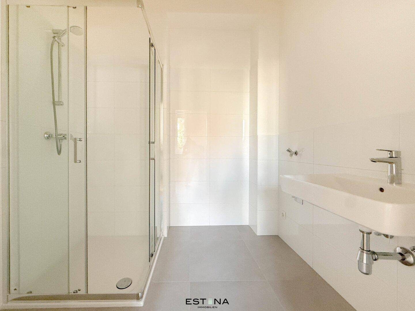 Modernes Badezimmer mit Duschkabine, weiß gefliesten Wänden und hellem Boden.