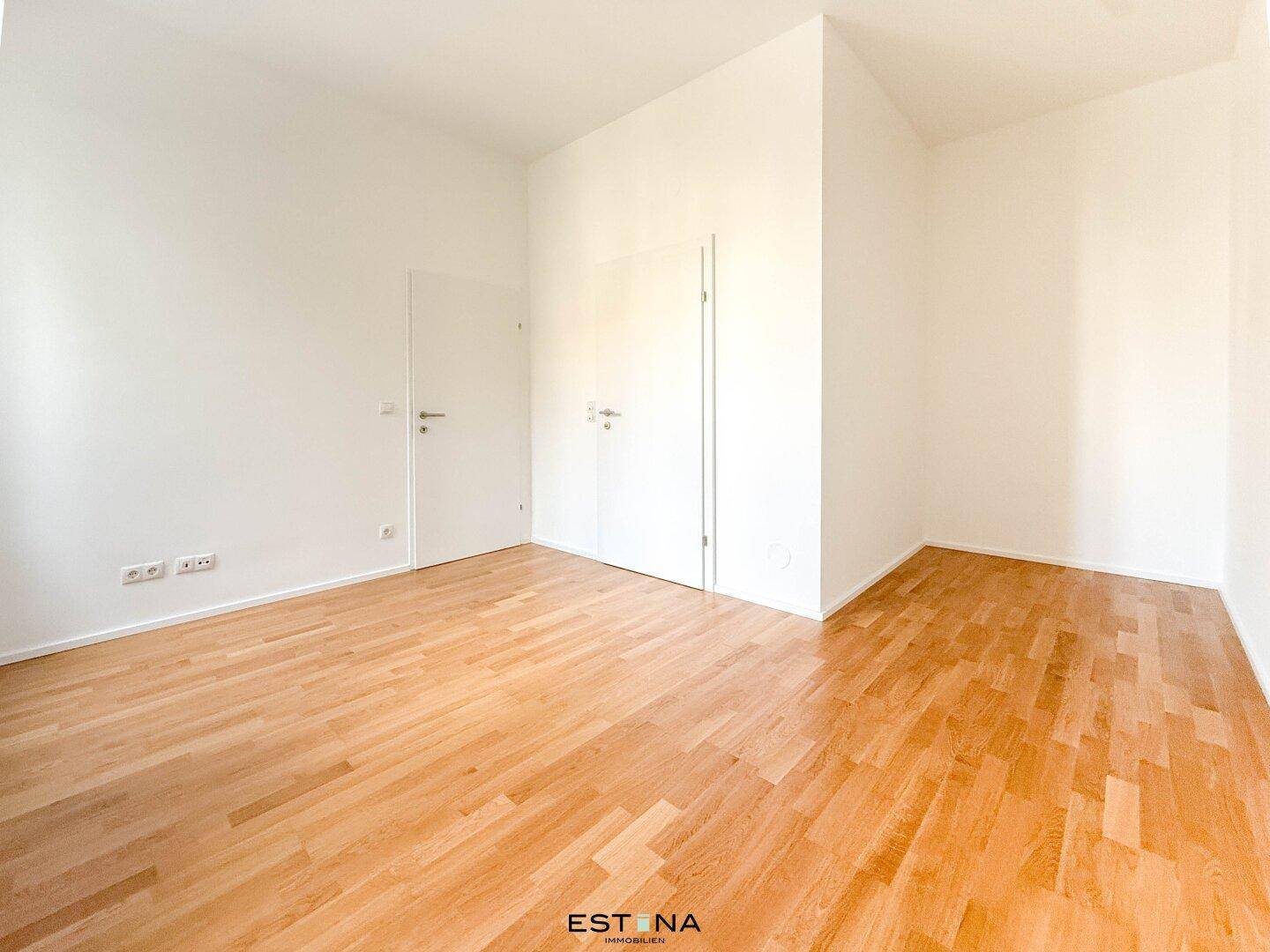 Geräumiges, helles Zimmer mit Parkettboden und weißen Wänden, ideal für Schlaf- oder Arbeitsbereich.