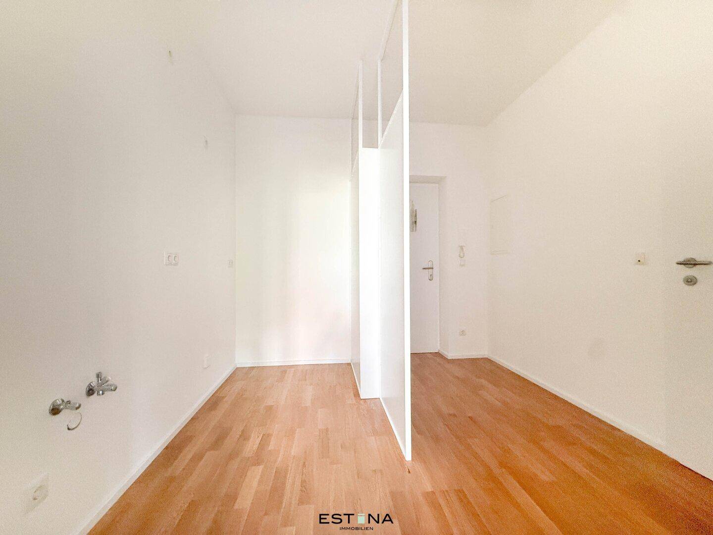 Helles, leeres Zimmer mit Parkettboden und einer modernen Raumtrennung, vielseitig nutzbar.