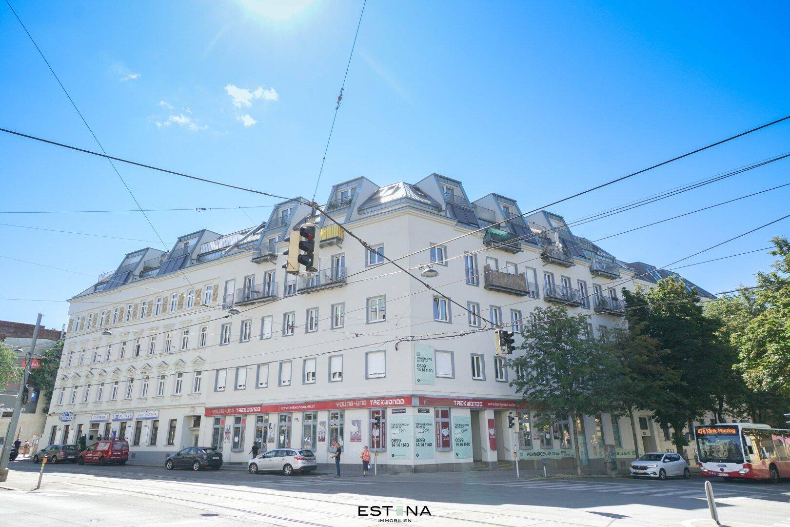 Großes Eckgebäude in städtischer Umgebung mit Geschäften im Erdgeschoss und Mansarddach.