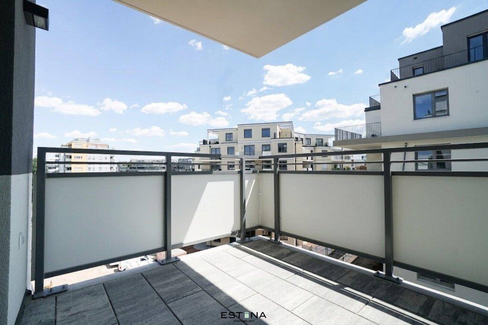 Geräumiger Balkon mit Fliesenboden und Blick auf moderne Wohngebäude unter blauem Himmel.