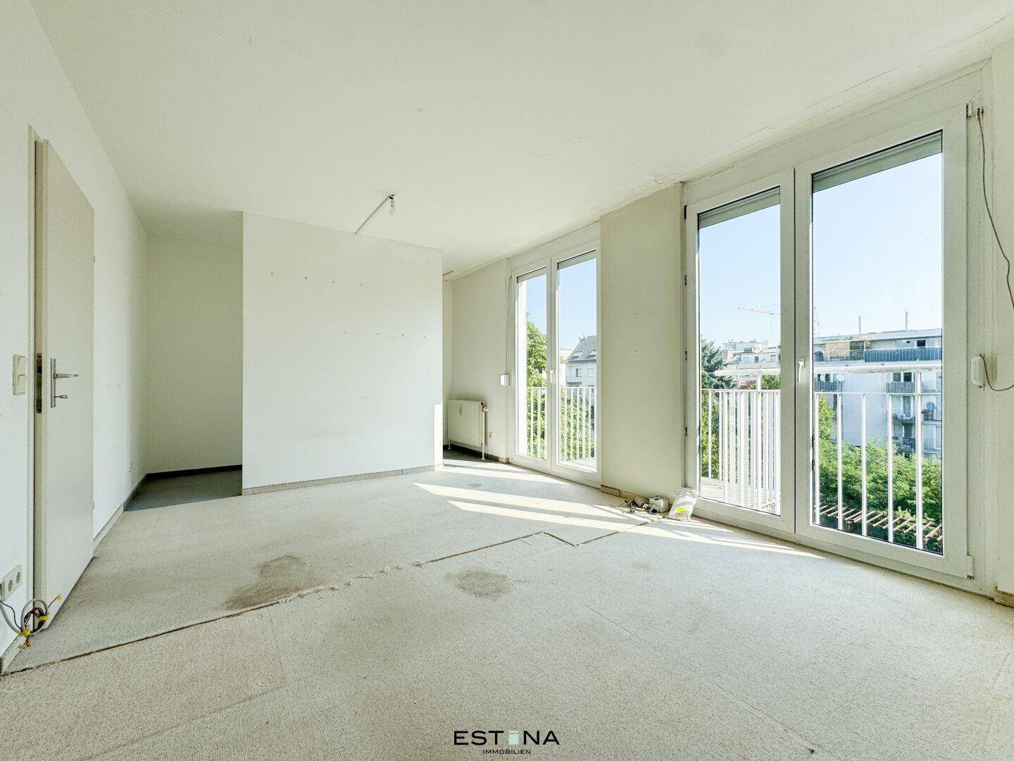 Heller Raum mit Teppichboden und großen Fenstern, die zu einem französischen Balkon führen.