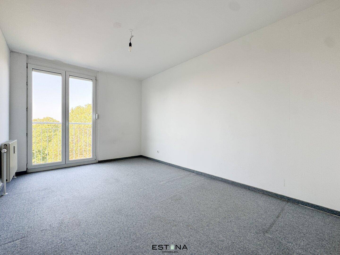 Schlafzimmer mit grauem Teppichboden und Zugang zu einem französischen Balkon, hell und funktional.