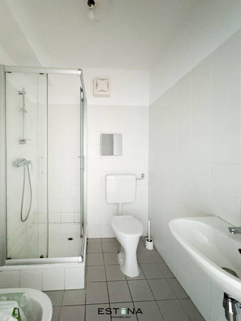 Badezimmer mit Duschkabine, Toilette, Waschbecken und weißen Wandfliesen, praktisch eingerichtet.
