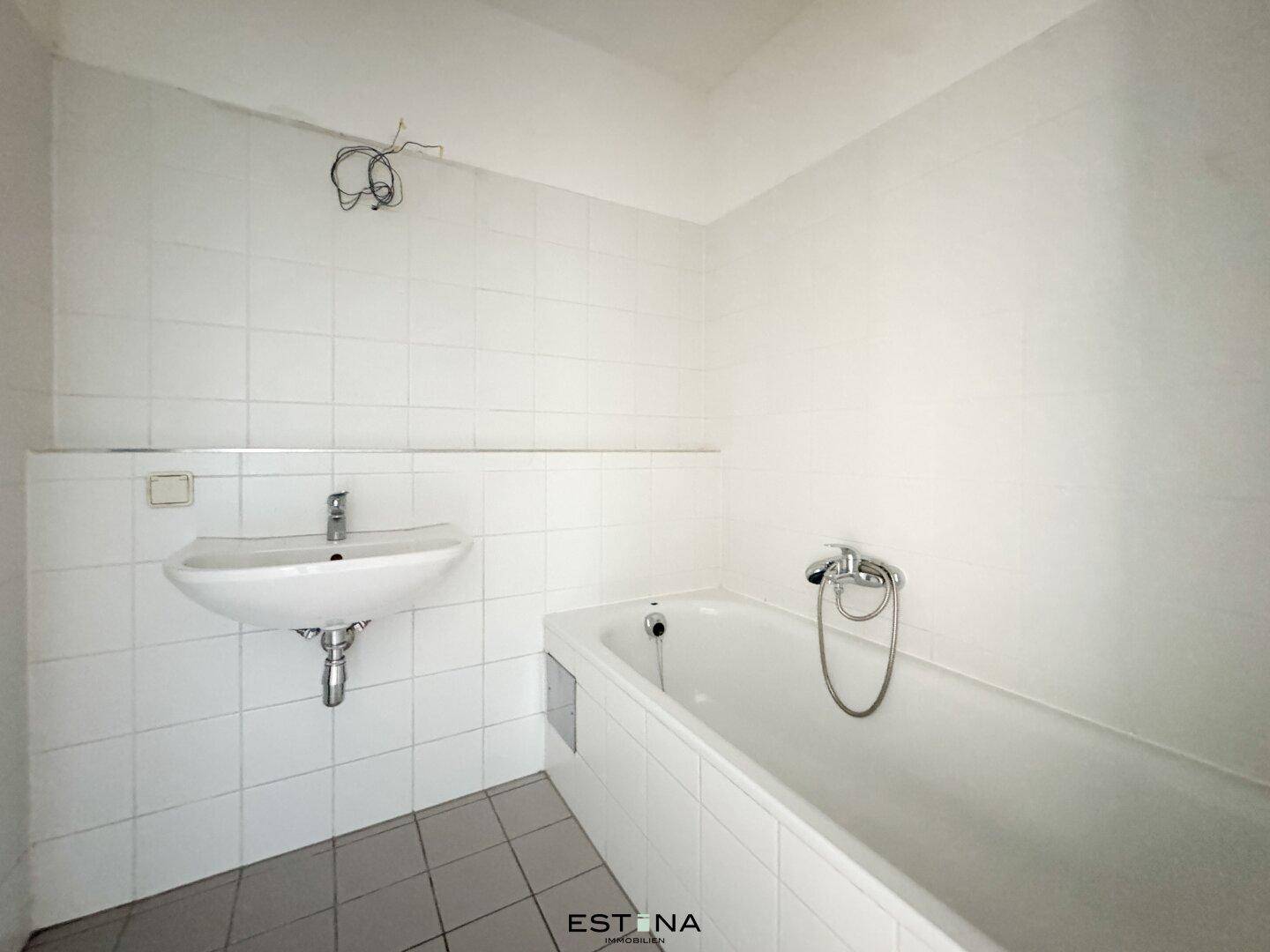 Badezimmer mit weißen Fliesen, Waschbecken und einer Badewanne, funktional und sauber.