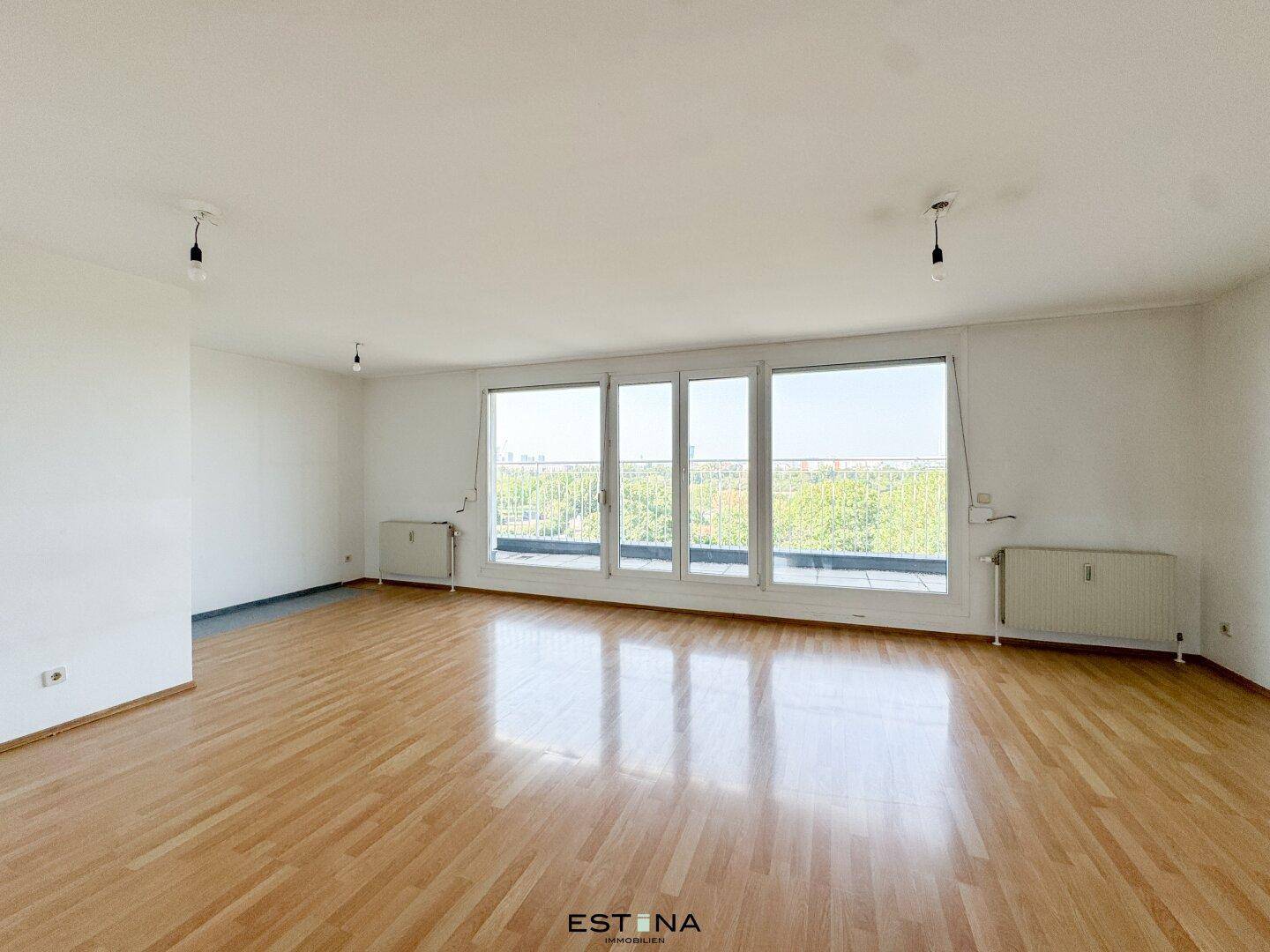 Helles Wohnzimmer mit großen Fenstern, glänzendem Parkettboden und viel natürlichem Tageslicht.