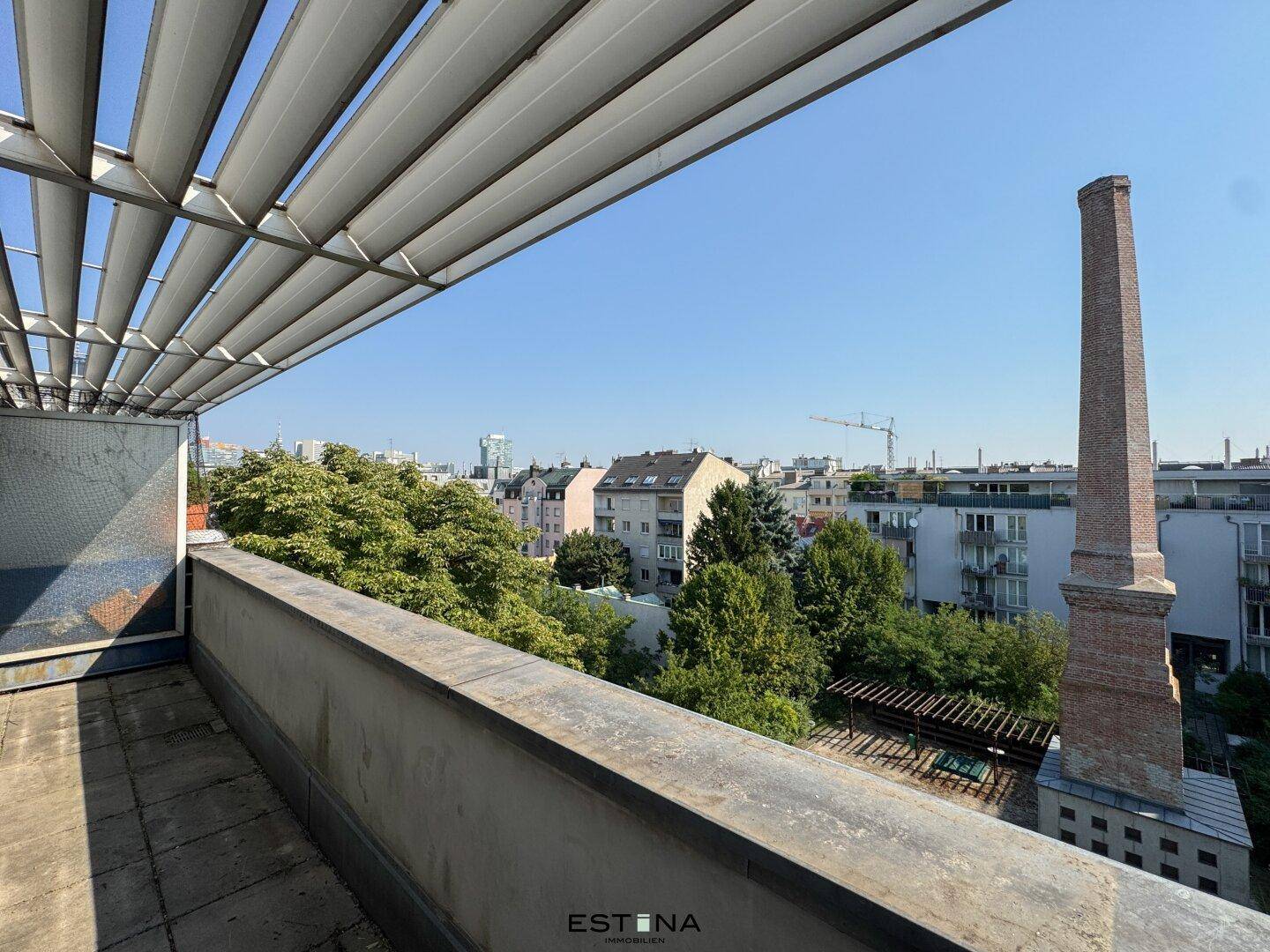 Geräumige Terrasse mit urbanem Ausblick und einem markanten Schornstein in der Ferne unter blauem Himmel.