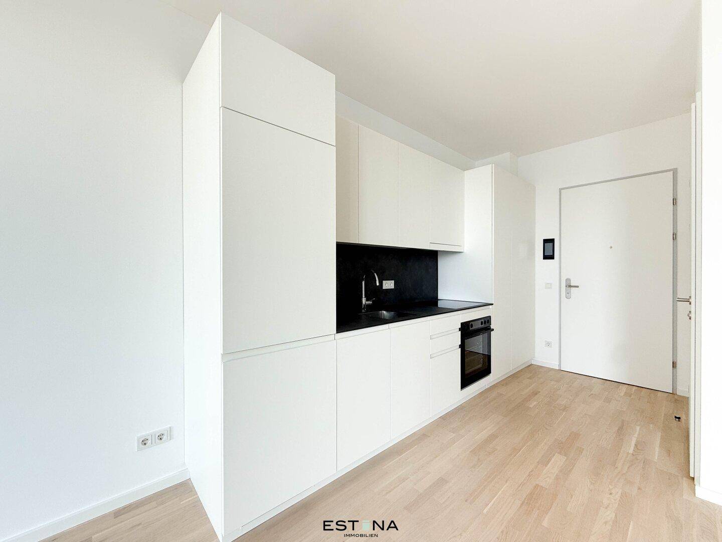 Moderne, weiße Einbauküche mit integriertem Backofen und dunkler Arbeitsplatte in minimalistischem Design.