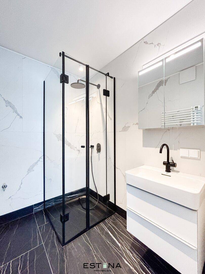 Modernes Badezimmer mit begehbarer Dusche, eleganten Marmorfliesen und schwarzer Armatur.