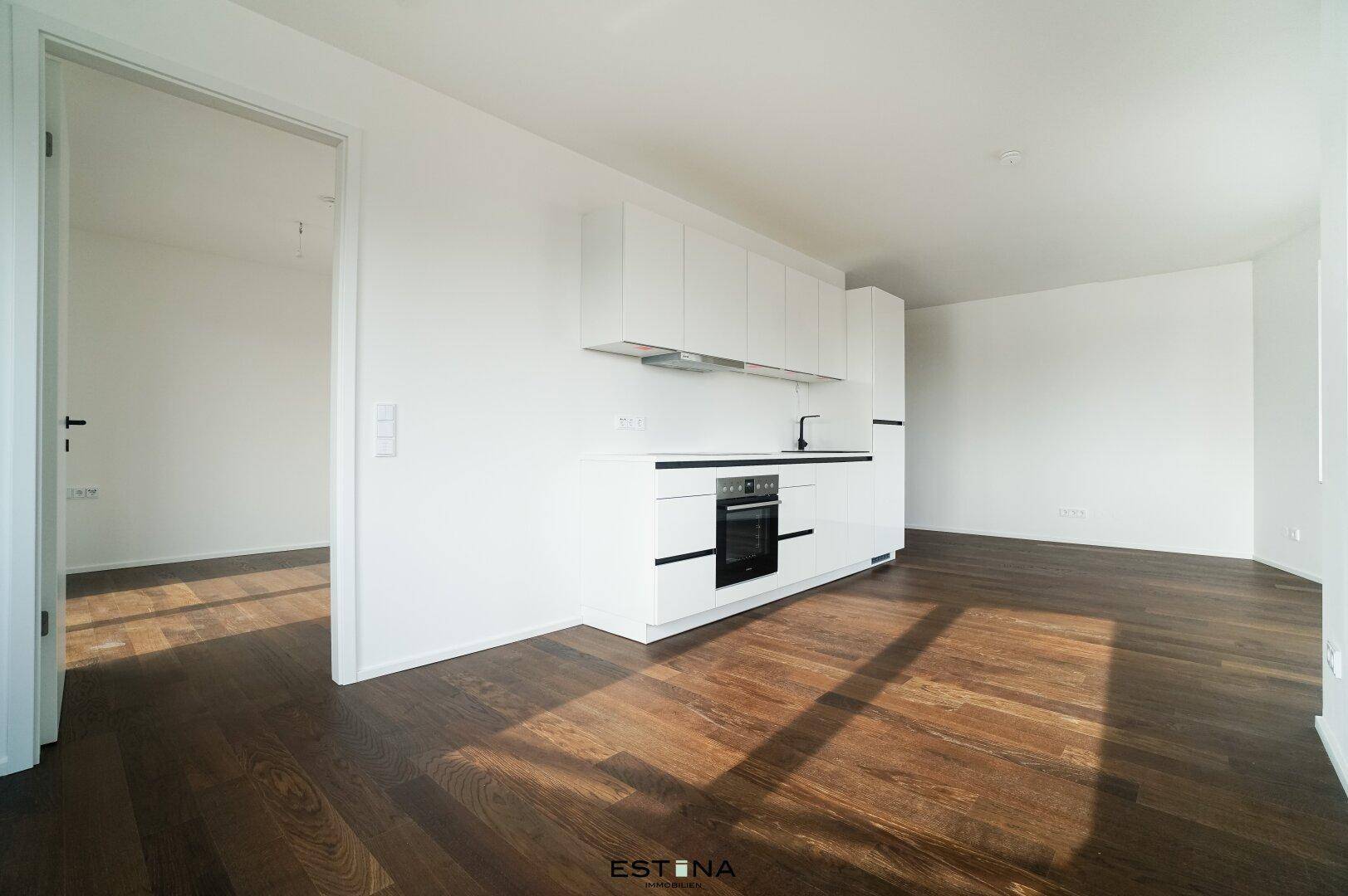 Heller Raum mit moderner, weißer Einbauküche und dunklem Holzboden, bereit zum Einzug.