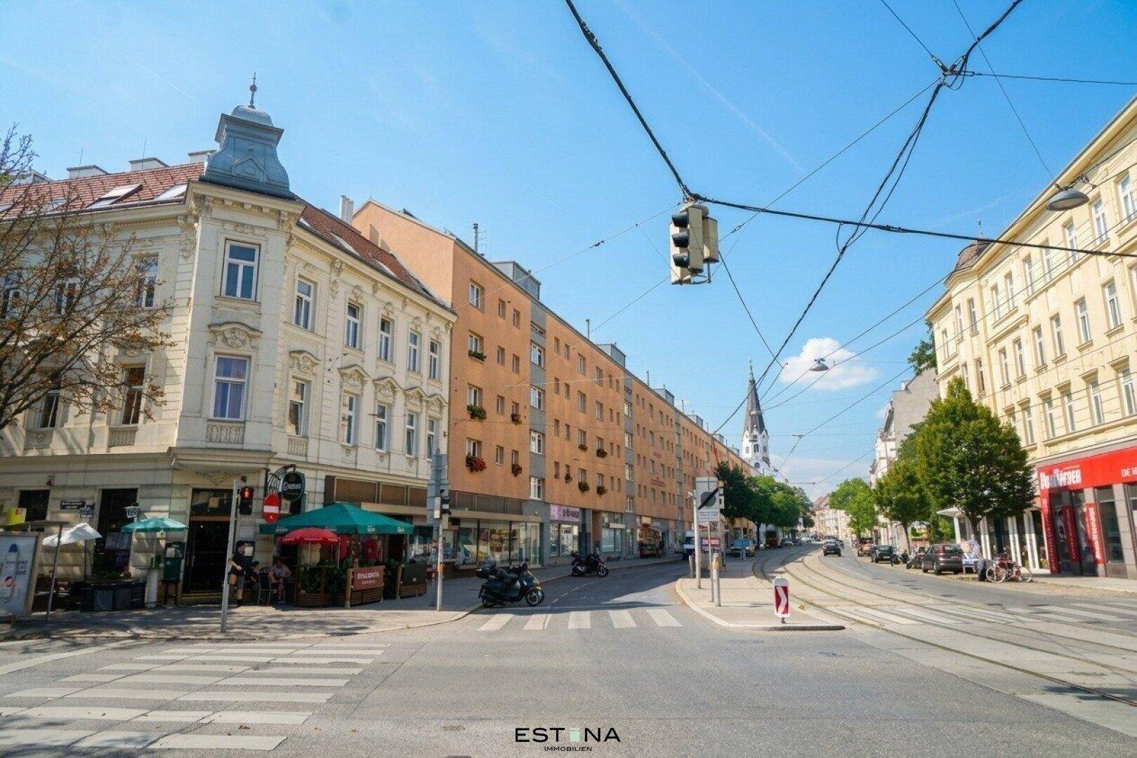 Belebte Stadtstraße mit verschiedenen Gebäuden, Geschäften und einer Kirche in der Ferne.