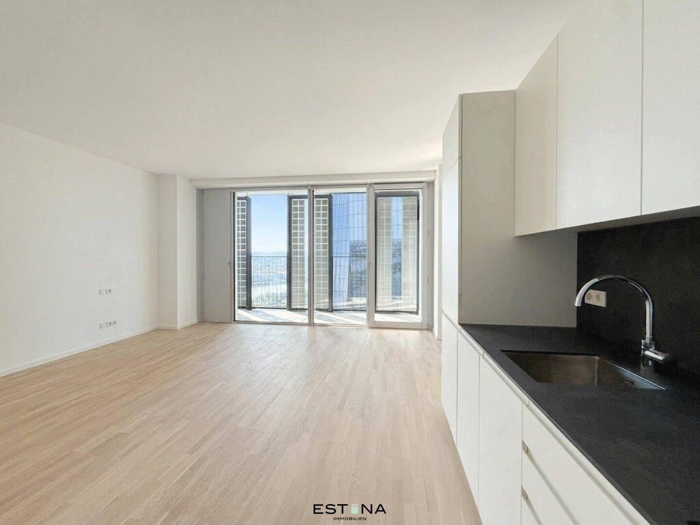 Heller offener Wohnbereich mit moderner Küche, hellem Parkettboden und Zugang zum Balkon mit Weitblick.