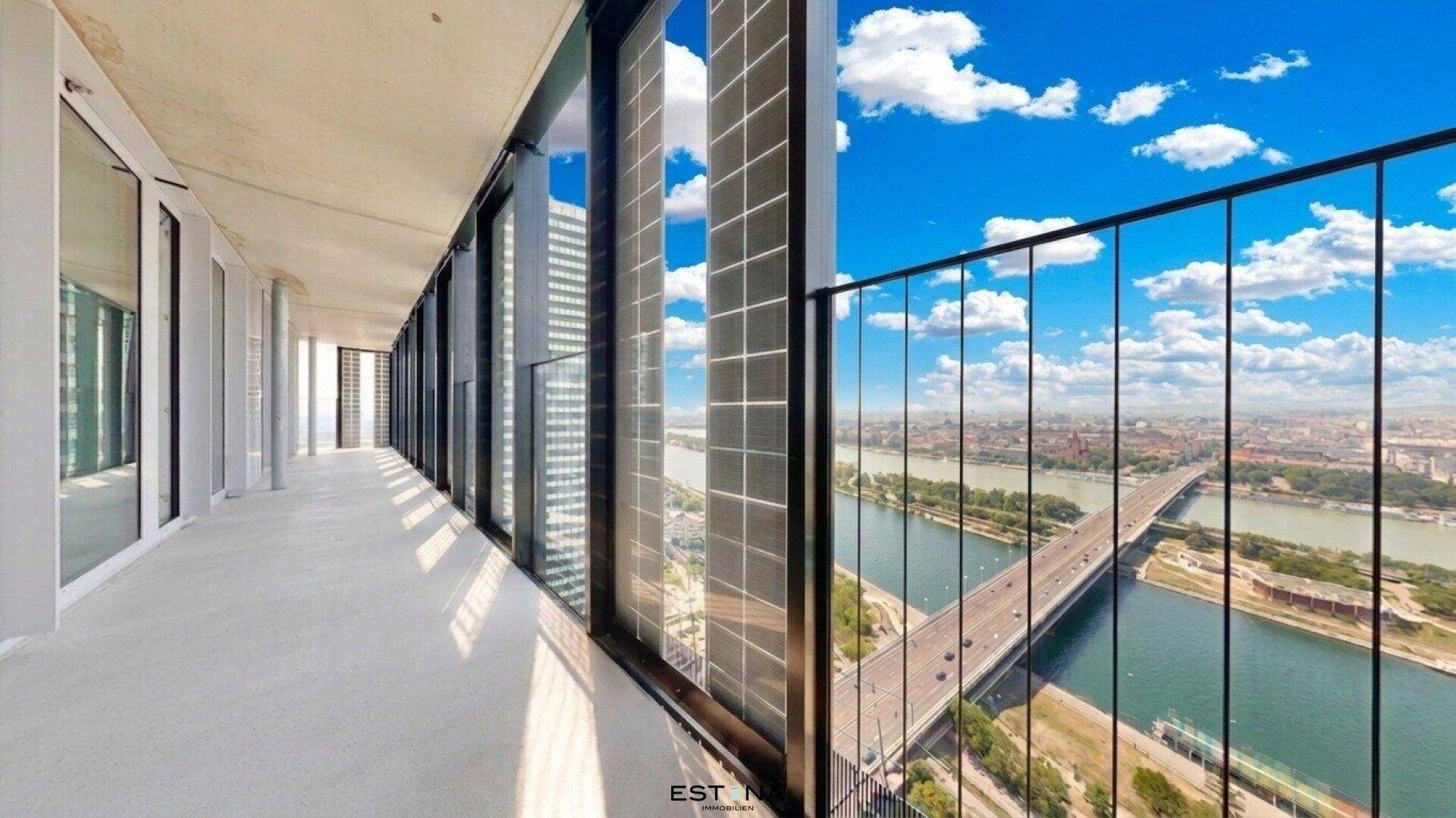 Lange Loggia mit Panoramablick auf die Stadt, den Fluss und eine Brücke unter blauem Himmel.