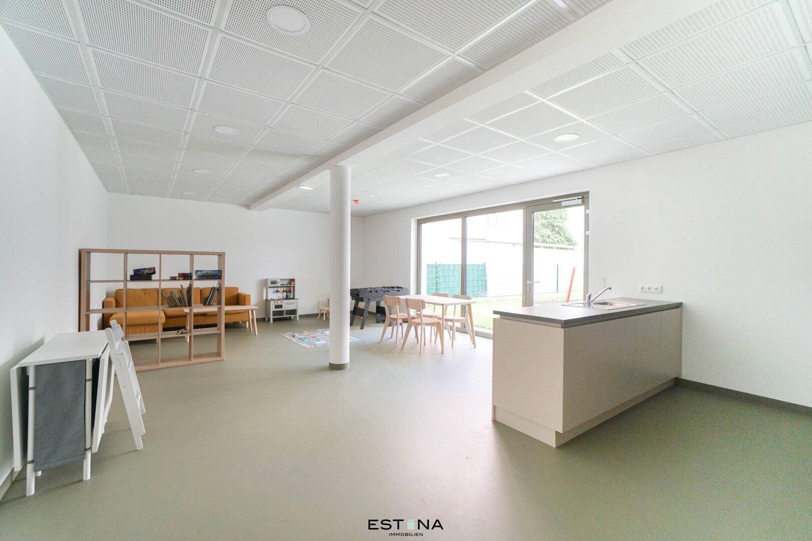 Großer Gemeinschaftsraum mit Sitzgelegenheiten, Esstisch und kleiner Küchenzeile.
