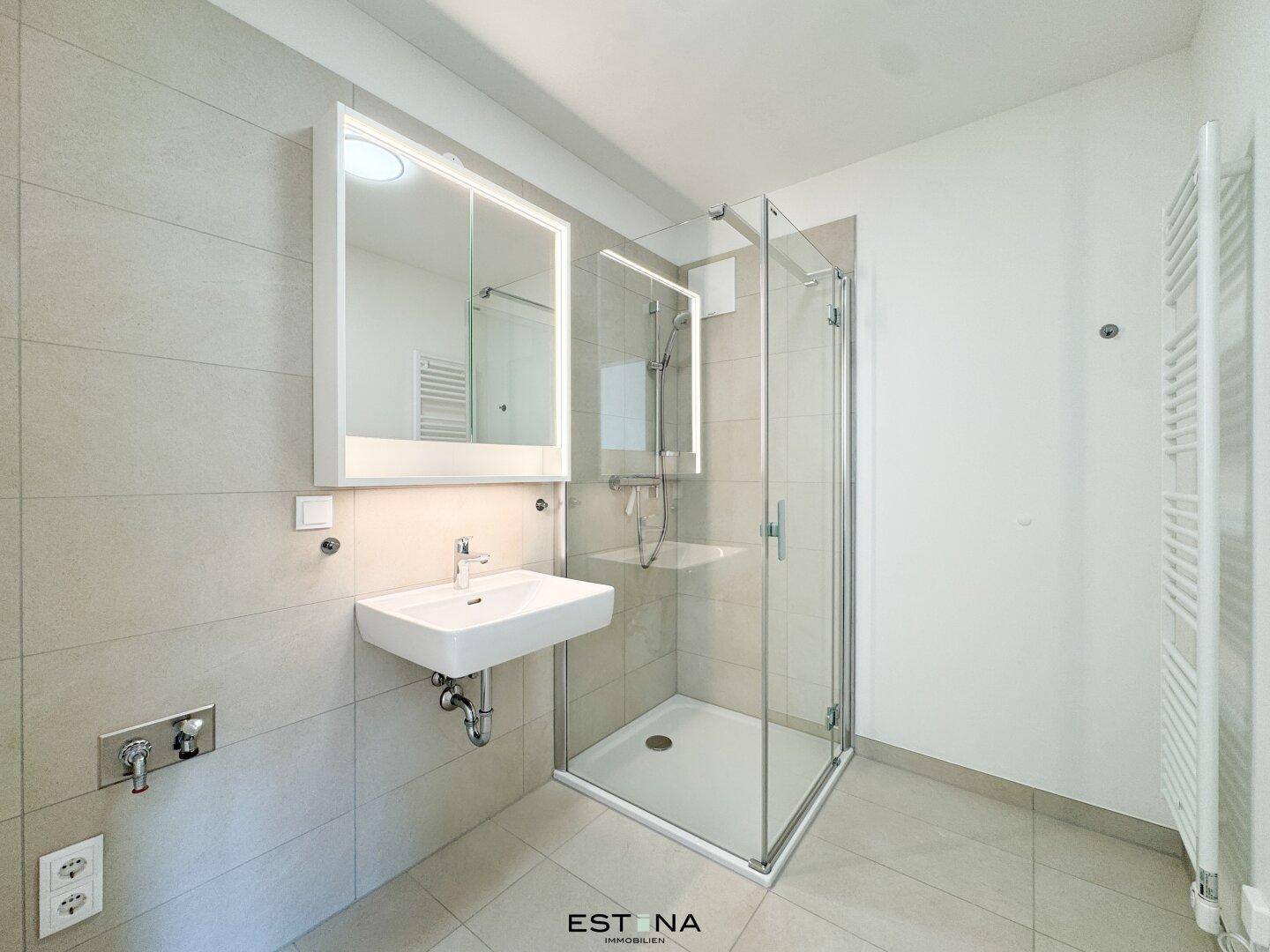 Modernes Badezimmer mit Duschkabine, Waschbecken, beleuchtetem Spiegelschrank und Handtuchheizkörper.