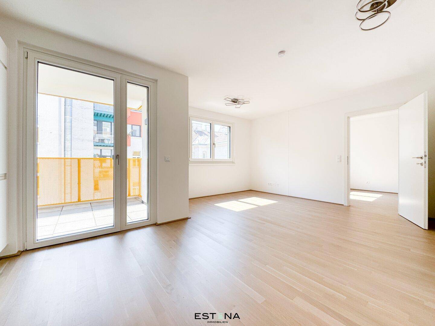 Helles Wohnzimmer mit Parkettboden, weißen Wänden und Zugang zu einem Balkon.