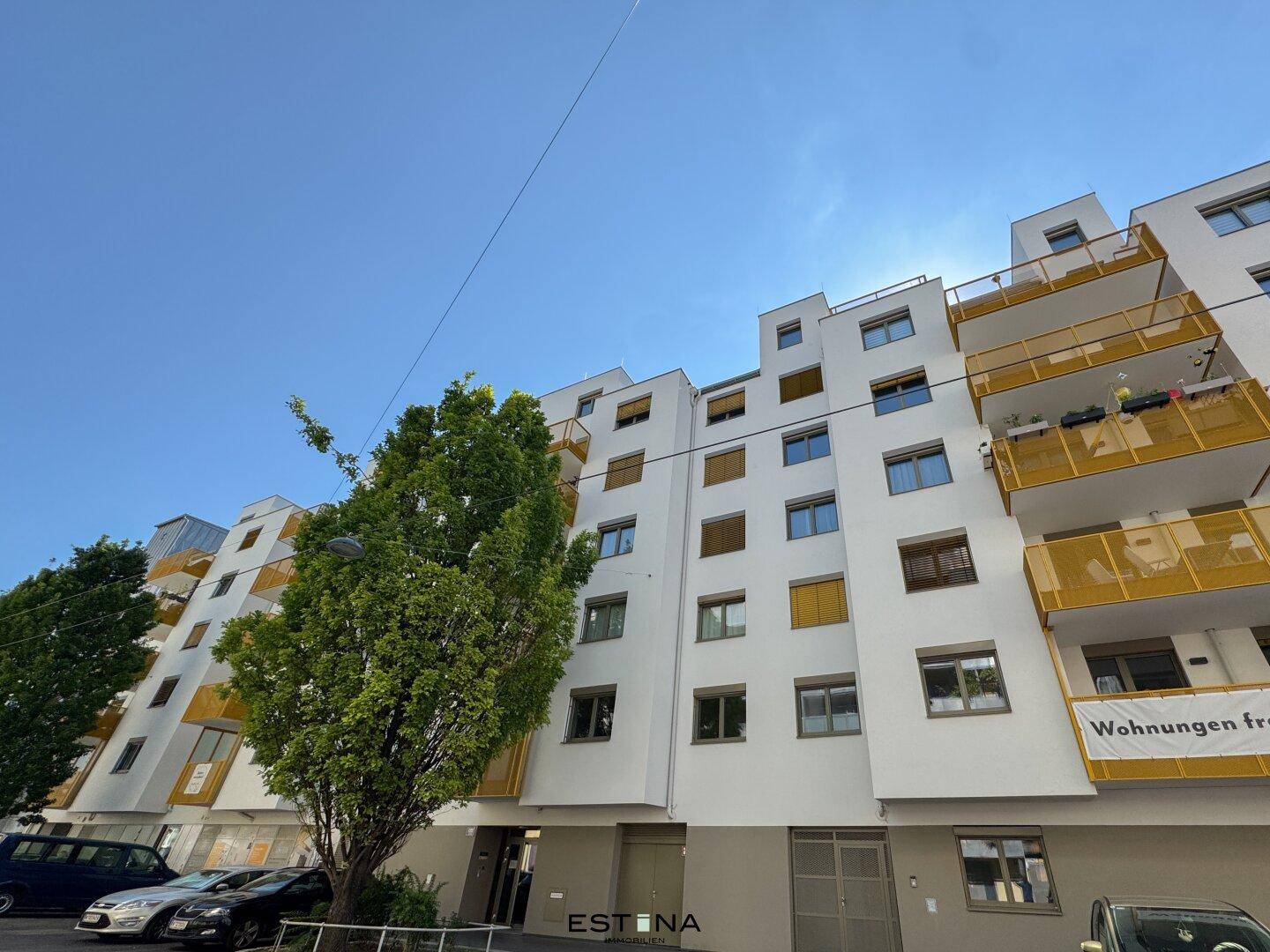 Moderne Wohnanlage mit weißer Fassade, großen Fenstern und gelben Balkonen unter blauem Himmel.
