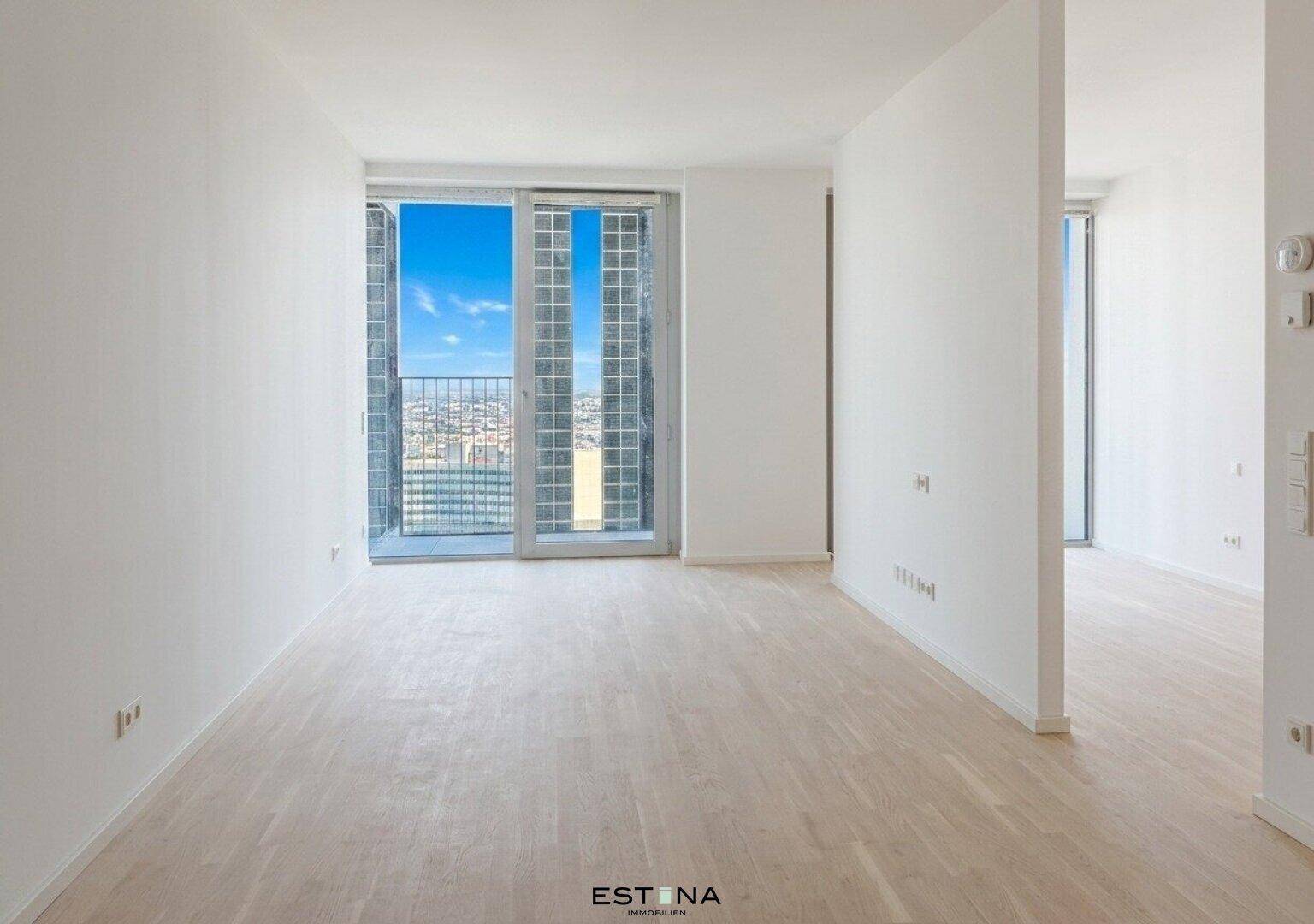 Helles, leeres Zimmer mit Parkettboden und Zugang zu einem Balkon oder einer Loggia.