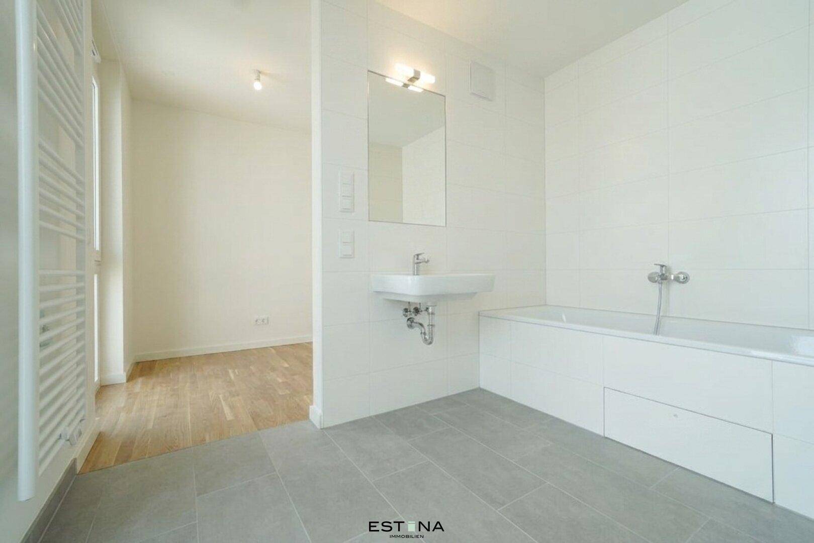 Modernes Badezimmer mit Badewanne, Waschbecken, beheiztem Handtuchhalter und hellen Fliesen.