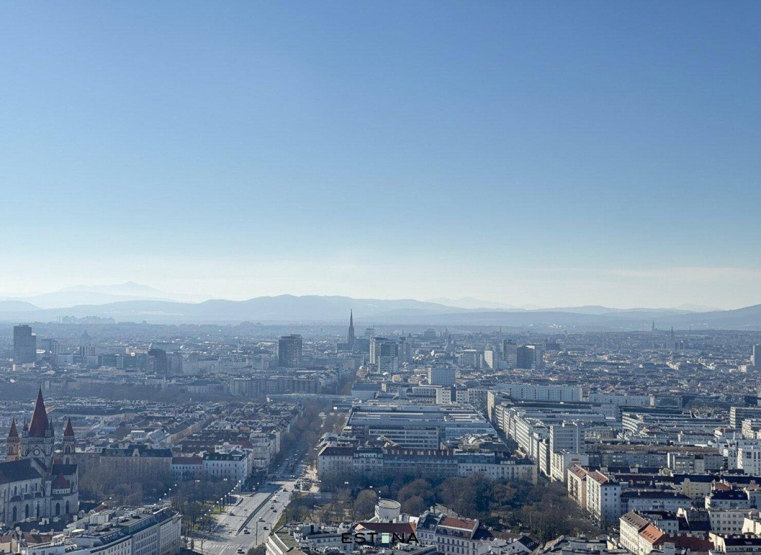 Weitläufiger Panoramablick über die Stadt mit ihrer Architektur und den umliegenden Bergen am Horizont.