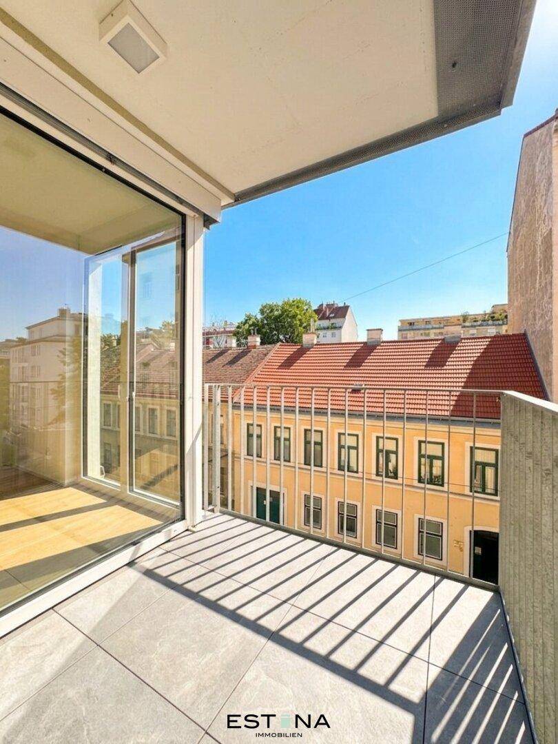 Sonniger Balkon mit Fliesenboden und Blick auf die Dächer der Stadt.
