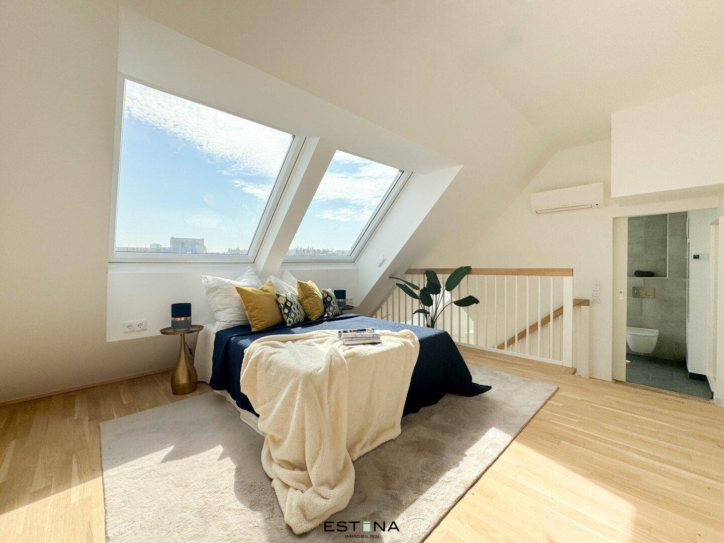 Helles Schlafzimmer mit großen Dachfenstern, Holzboden und direktem Zugang zum Badezimmer.