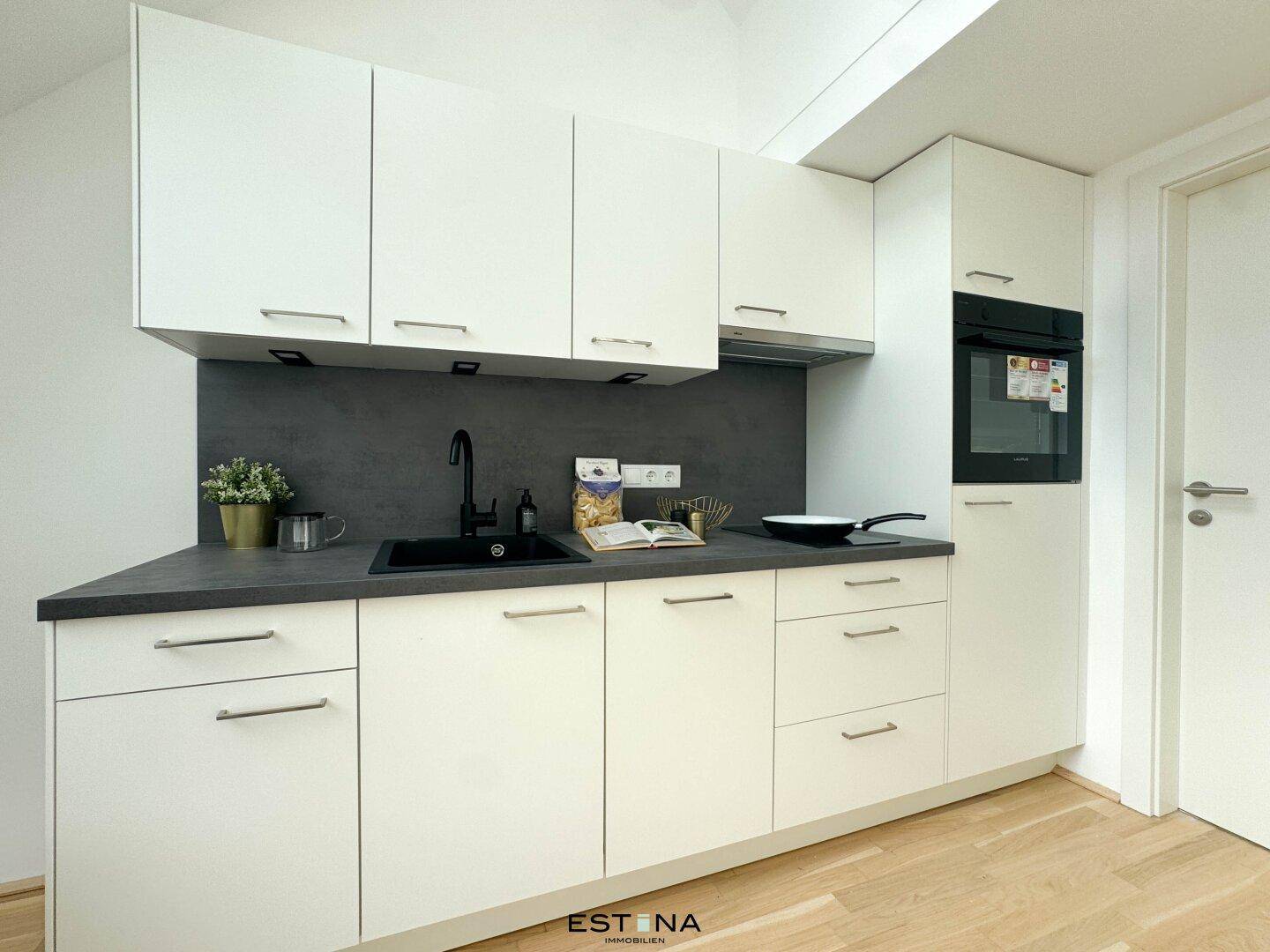 Moderne Einbauküche mit weißen Schränken, dunkler Arbeitsplatte und integriertem Backofen.