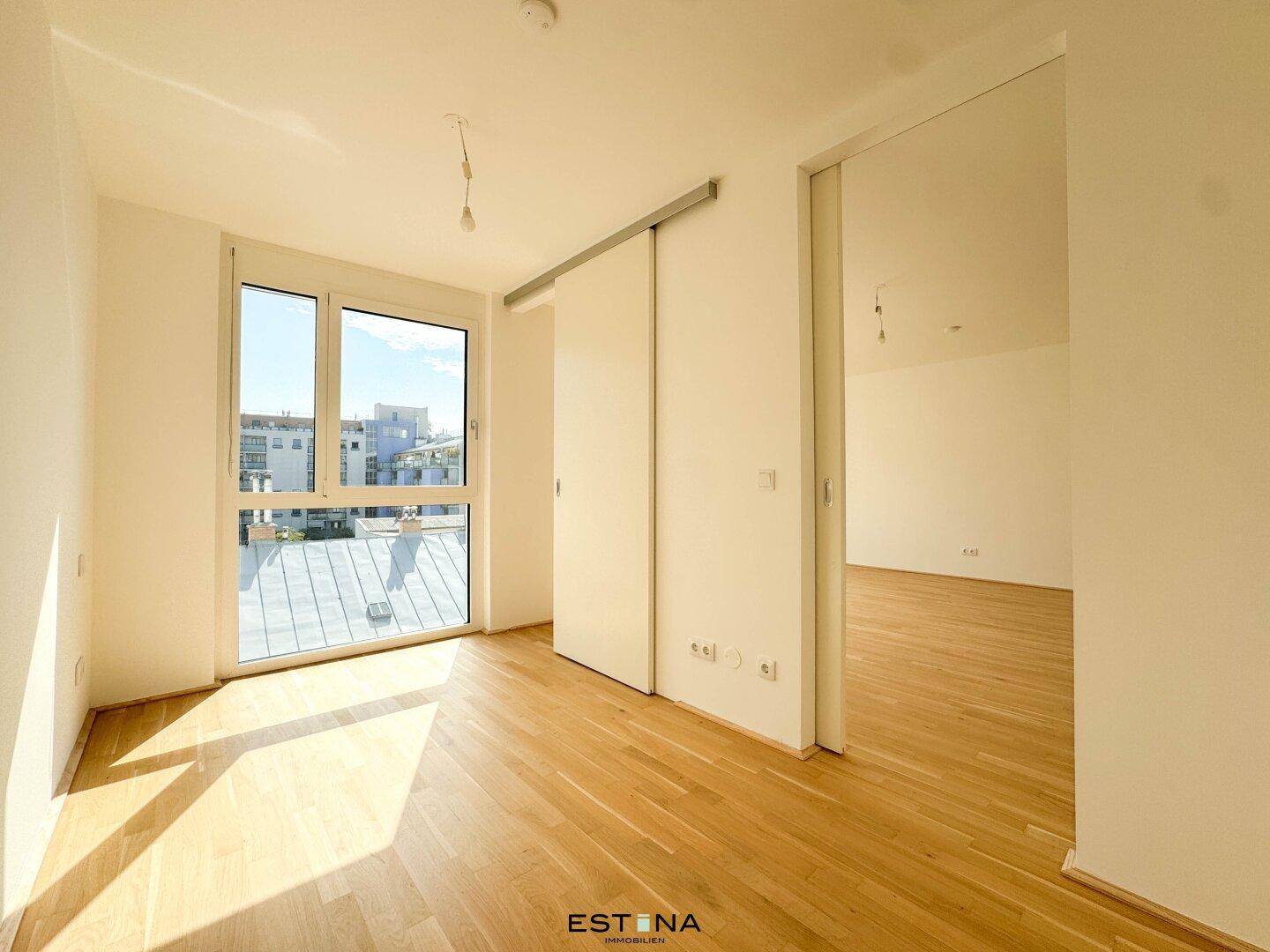 Schlafzimmer mit großen Fenstern, Parkettboden und viel natürlichem Licht.