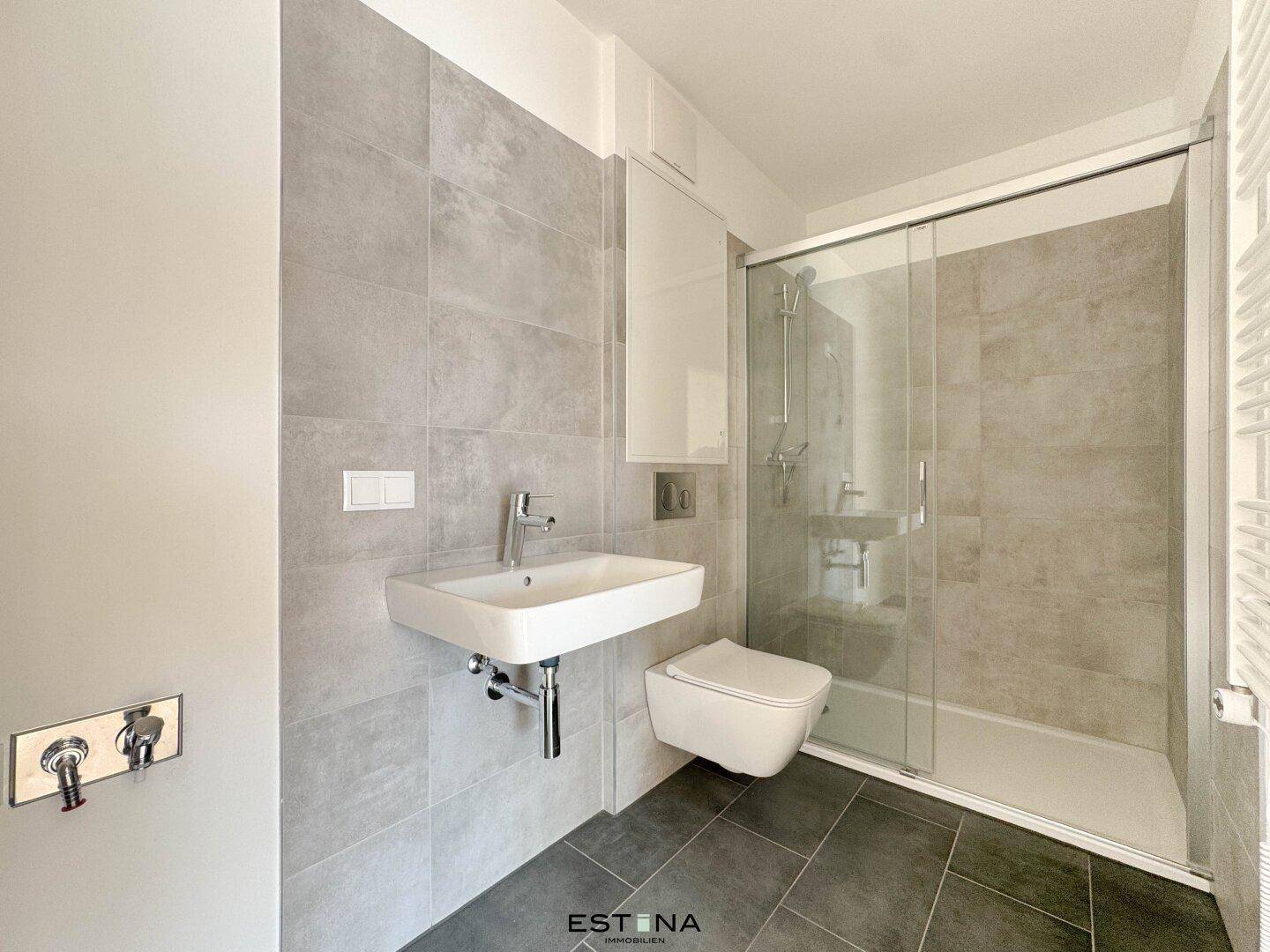 Modernes Badezimmer mit grauen Fliesen, Dusche und wandhängendem WC.