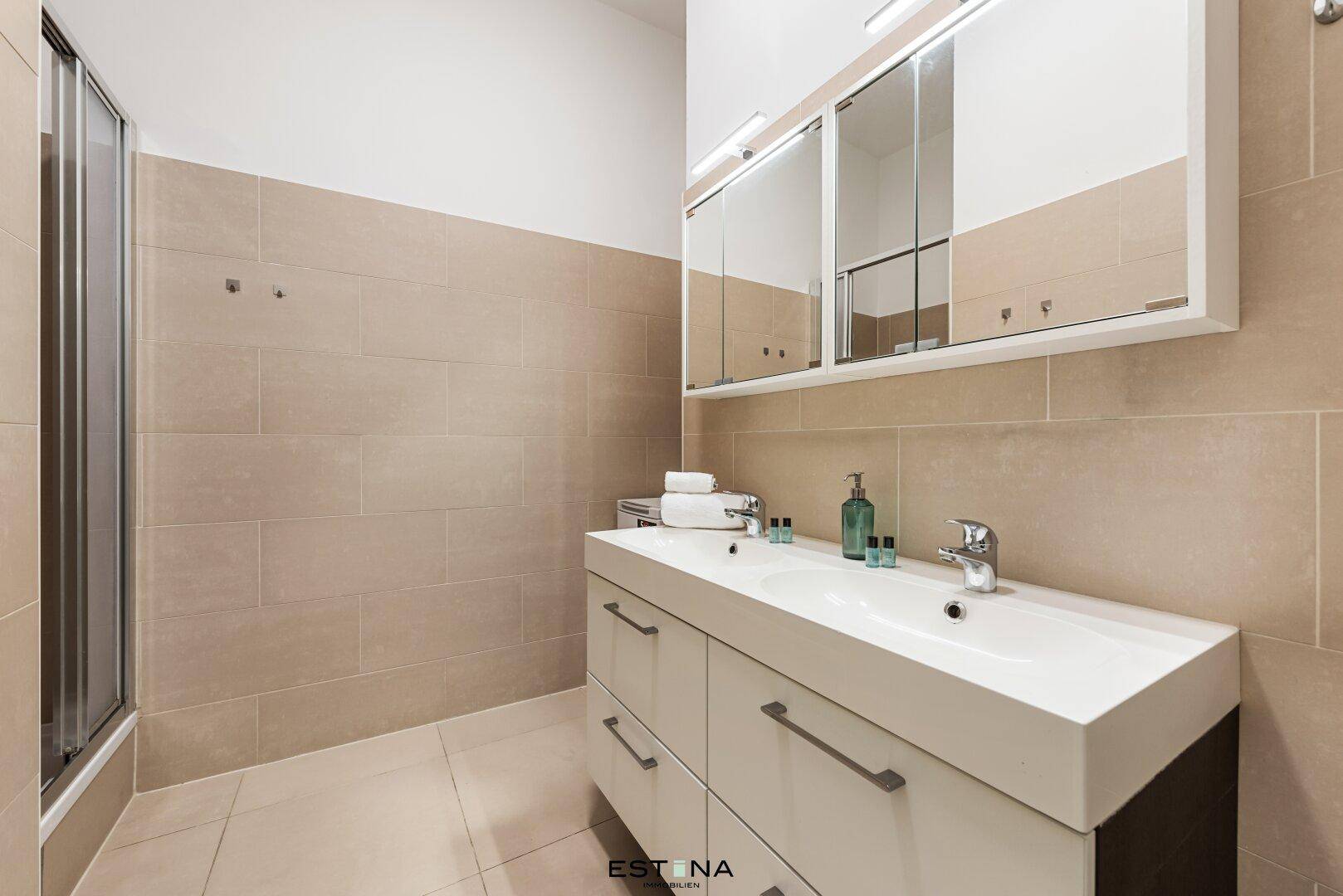 Modernes Badezimmer mit Doppelwaschbecken, Spiegelschrank und Duschkabine, in hellen Beigetönen gehalten.