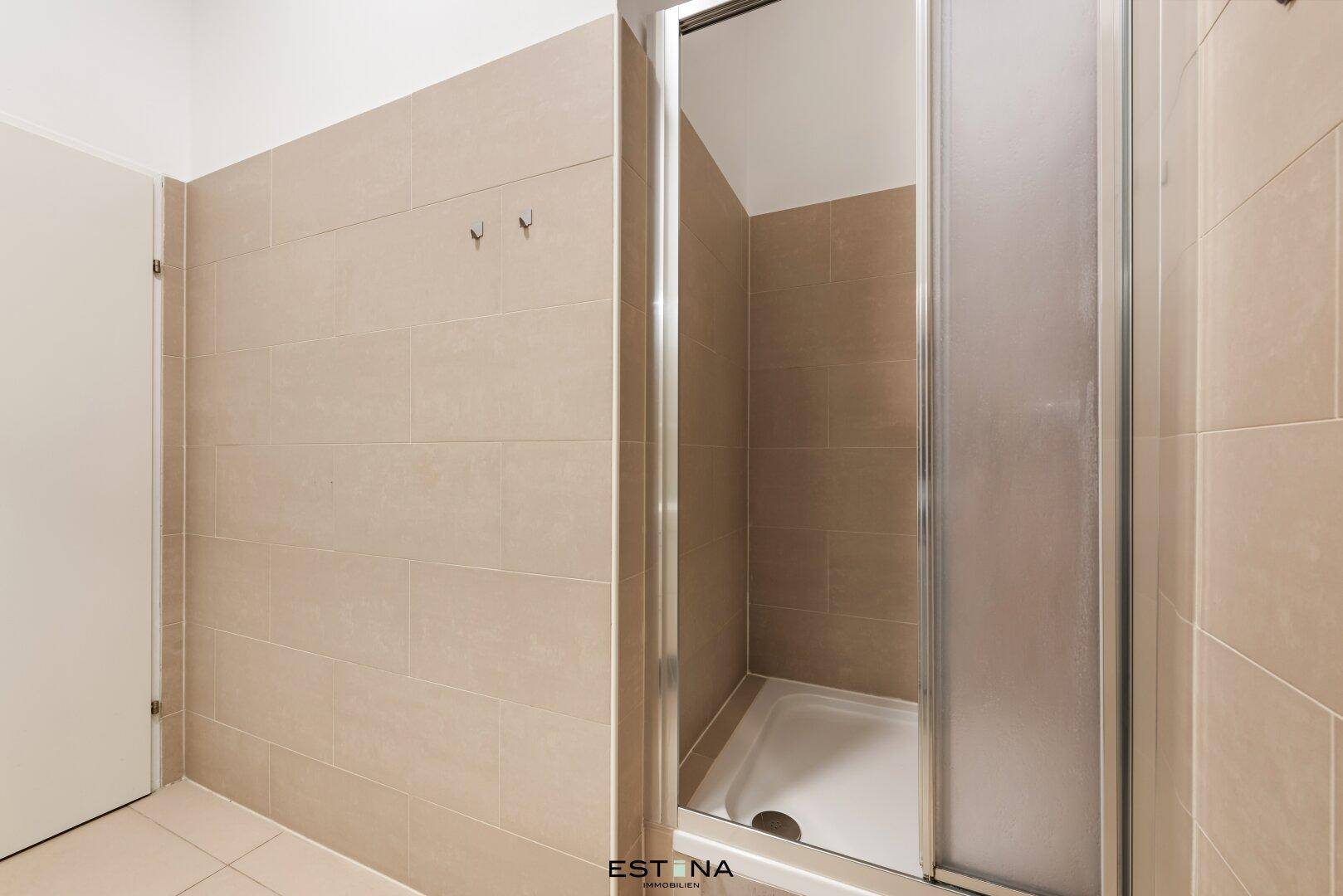 Duschbereich im modernen Badezimmer mit hellen Fliesen und Glastür, bietet eine erfrischende Dusche.