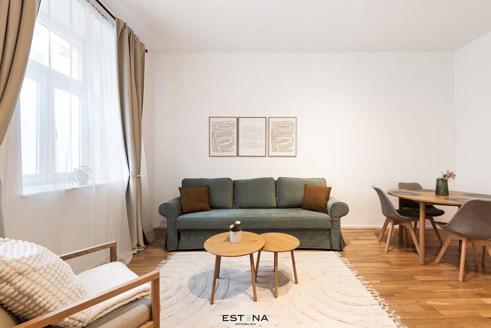 Gemütlicher Wohnbereich mit beigem Sofa, Holztischen und großen Fenstern für viel Tageslicht.