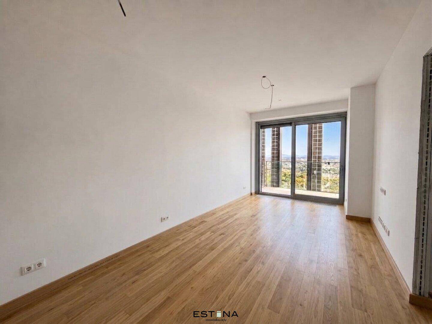 Helles Zimmer mit Holzfußboden, großen Schiebetüren und Zugang zu einem Außenbereich.