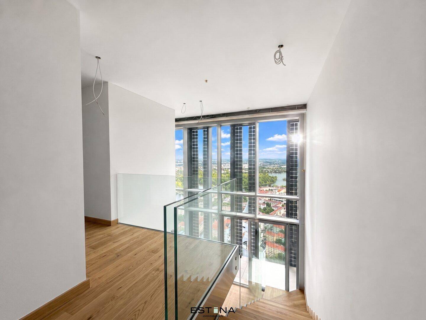 Moderner Treppenaufgang mit Glasgeländer und großen Fenstern, die einen weiten Stadtblick ermöglichen.