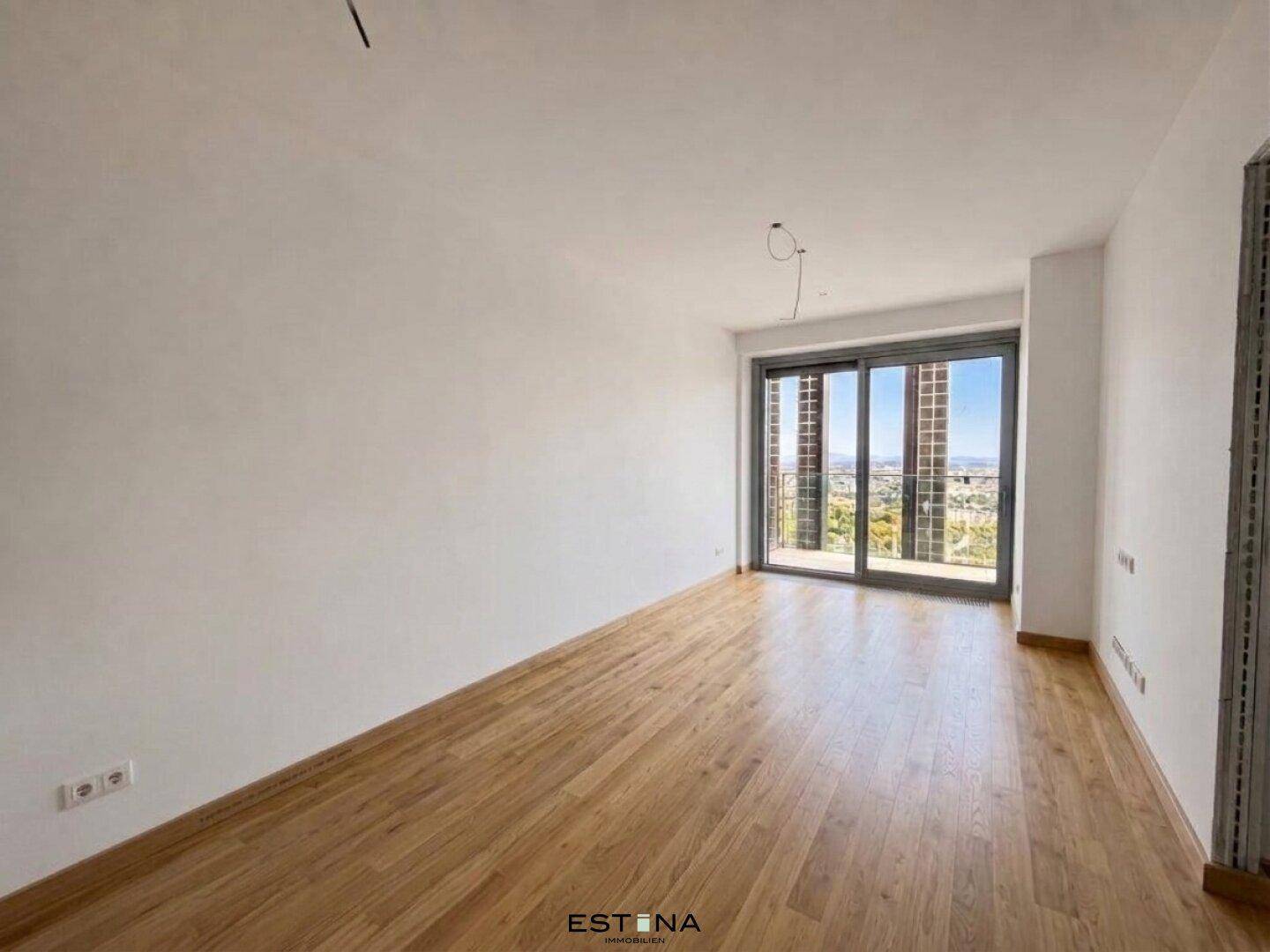 Heller Raum mit Holzboden und großen Schiebetüren, die Zugang zu einem Außenbereich bieten.