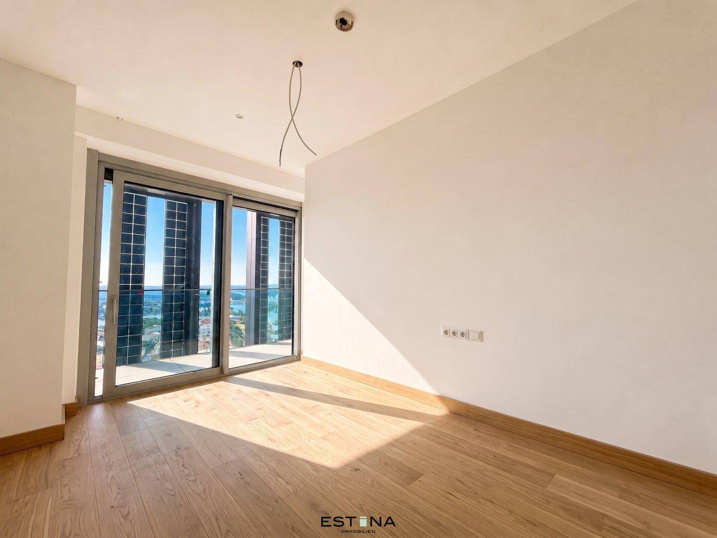 Helles Schlafzimmer mit Holzboden und Schiebetüren zu einem Balkon mit Stadtblick.