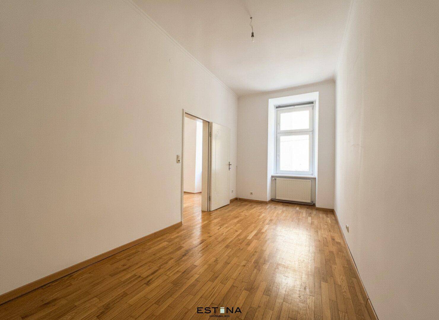 Geräumiges, helles Zimmer mit Holzboden und einem Fenster, ideal für Wohn- oder Schlafbereich.