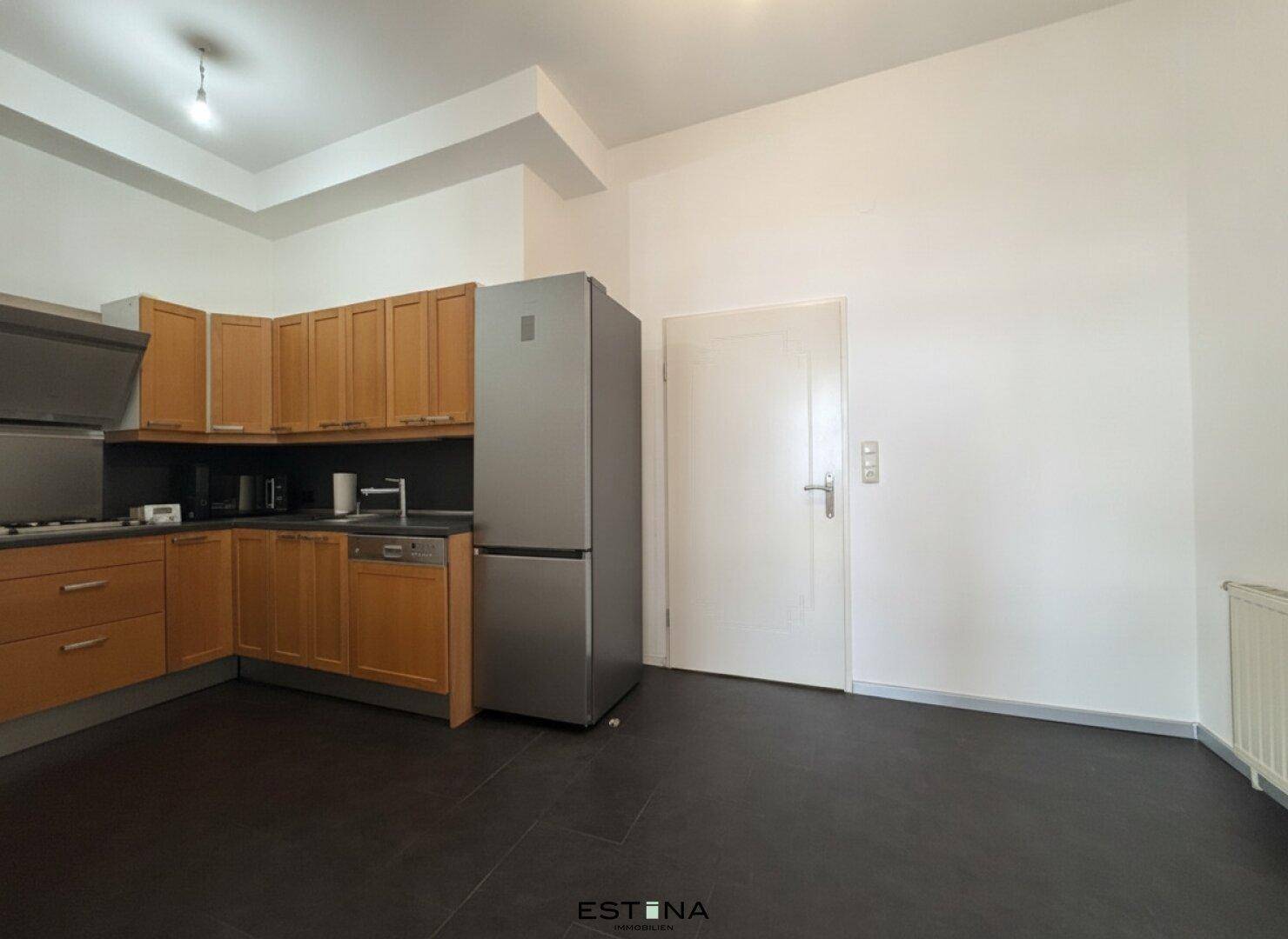 Funktionale Küche mit Holzschränken, dunklem Fliesenboden und integrierten Geräten.