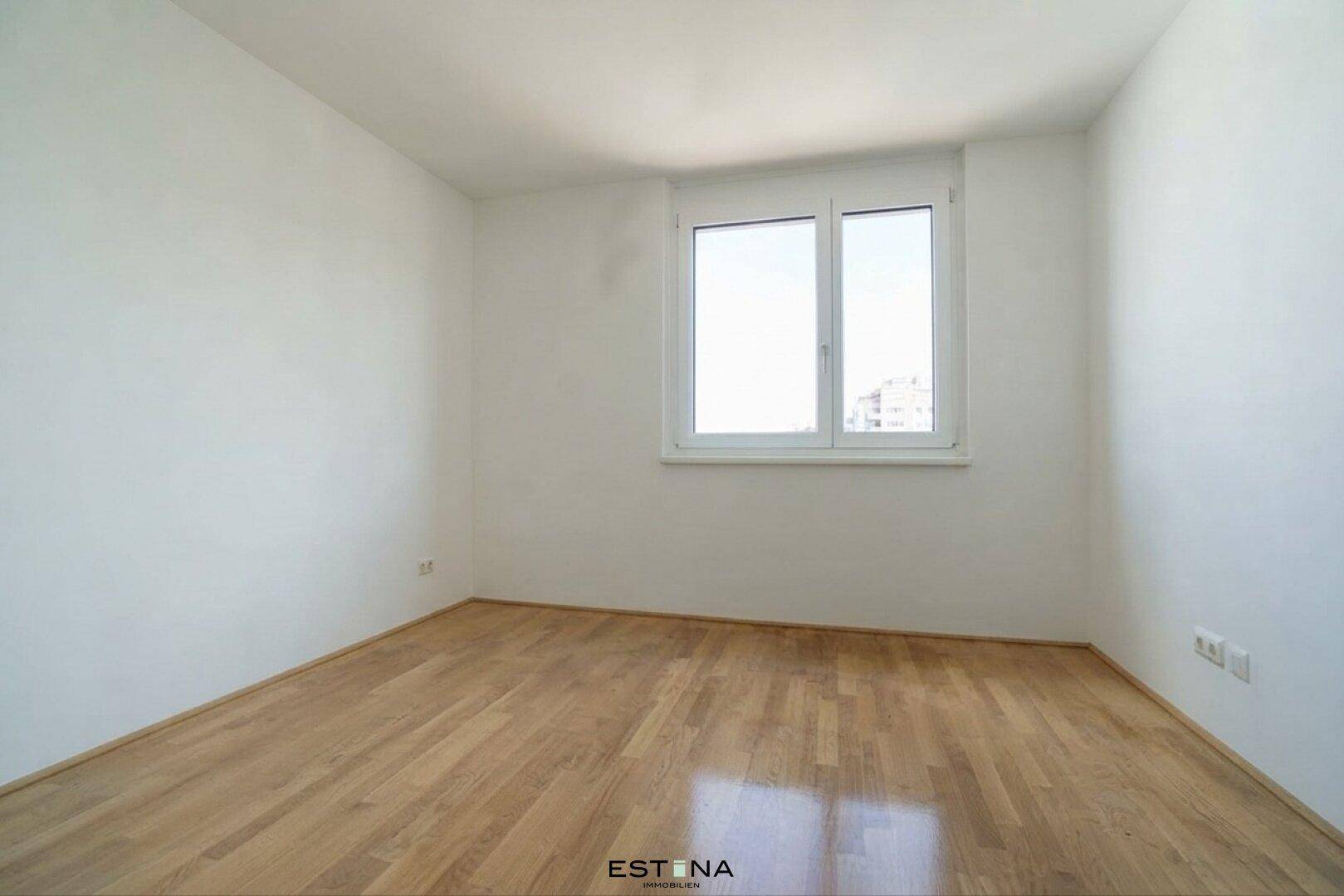 Leeres Schlafzimmer mit hellen Wänden, Holzboden und einem Fenster für natürliches Licht.